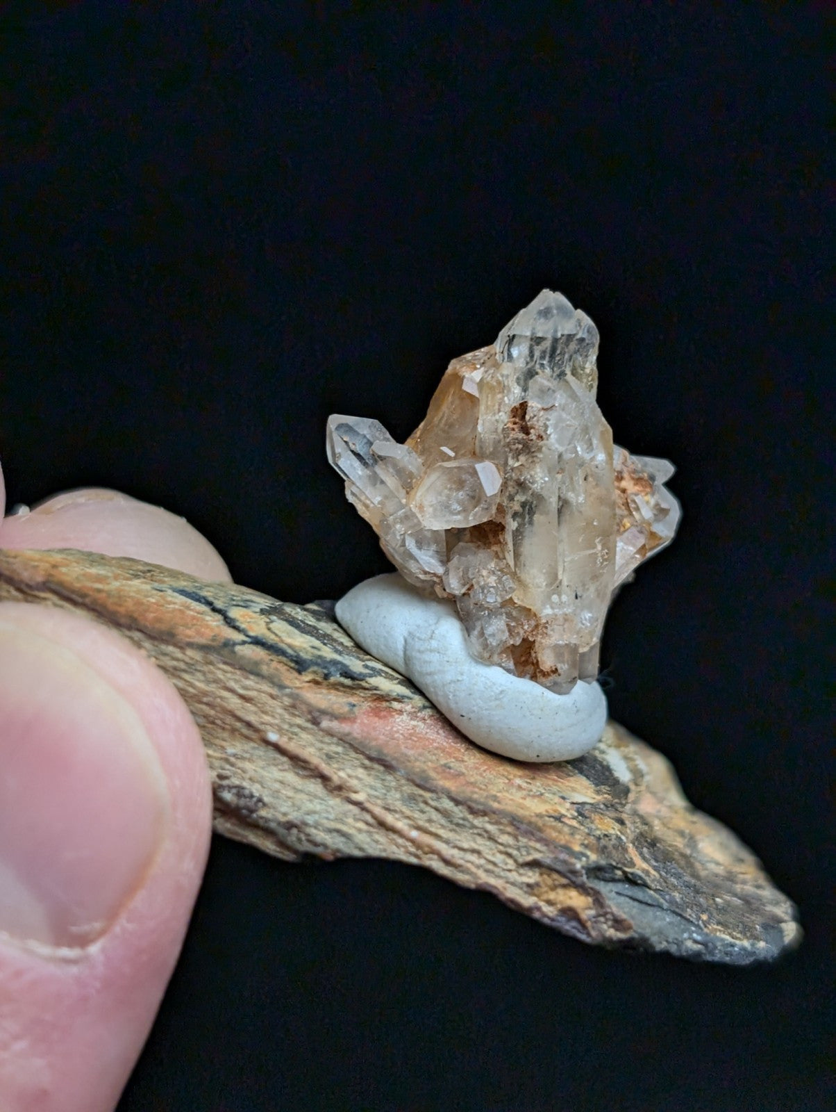 A translucent, multi-faceted quartz crystal cluster with subtle amber and grayish hues rests atop a smooth, pale blue ceramic base.