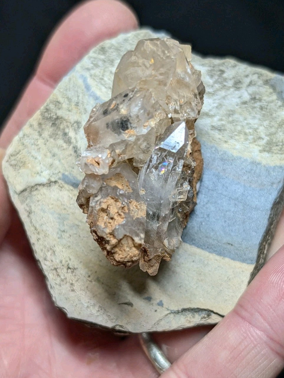A cluster of translucent, clear quartz crystals with subtle golden inclusions and sharp facets rests on a textured gray rock base.
