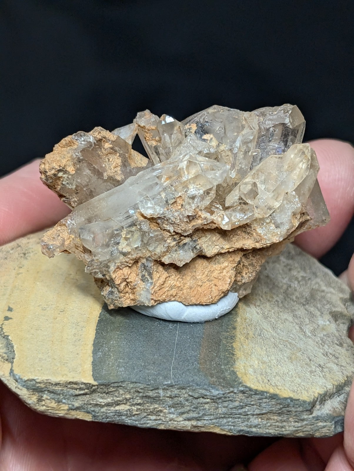A cluster of translucent quartz crystals with golden-brown matrix rock, displayed on a flat stone slab.