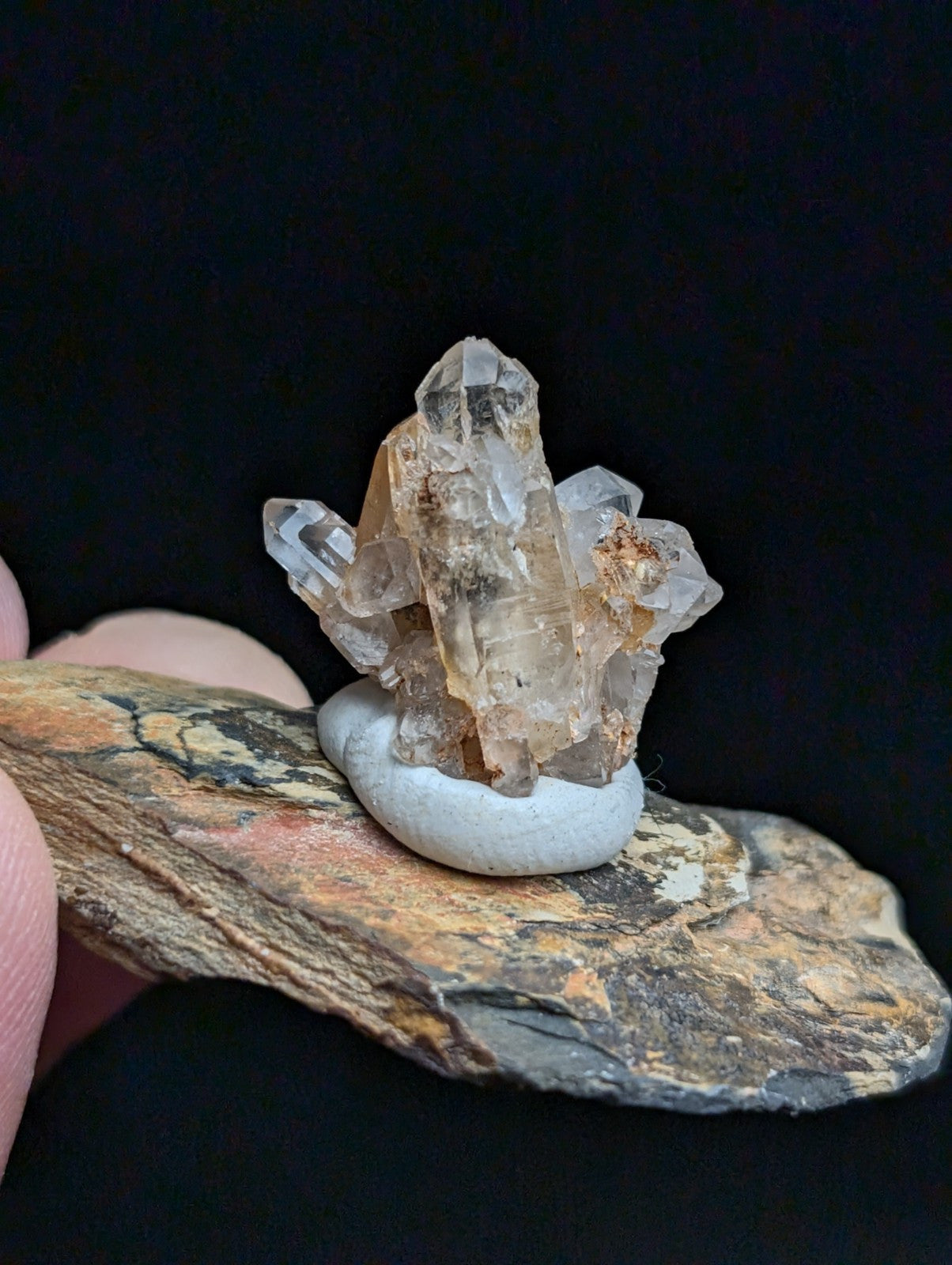 A translucent, multi-faceted quartz crystal cluster with amber and clear hues rests atop a smooth white base.