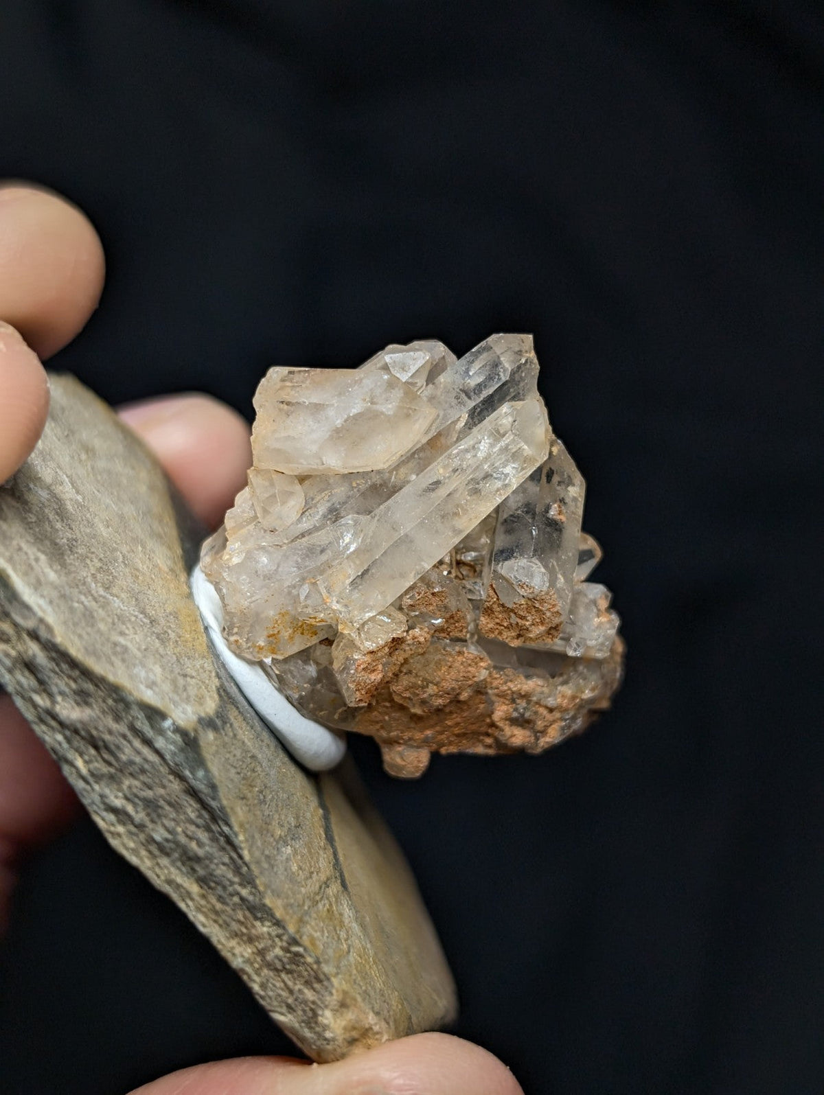 A cluster of translucent, pale quartz crystals with sharp edges and a slightly cloudy appearance, embedded in a rough brownish matrix.