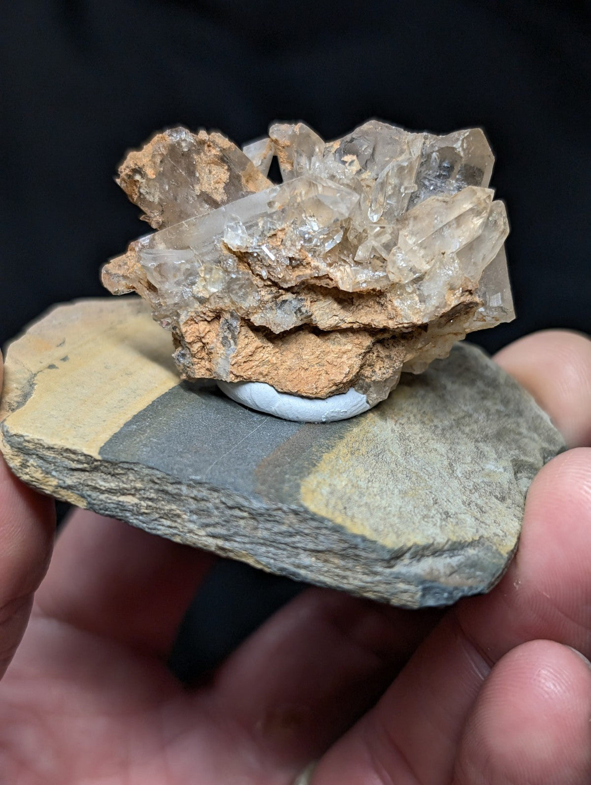 A cluster of translucent quartz crystals with earthy brown matrix, mounted on a flat stone slab.