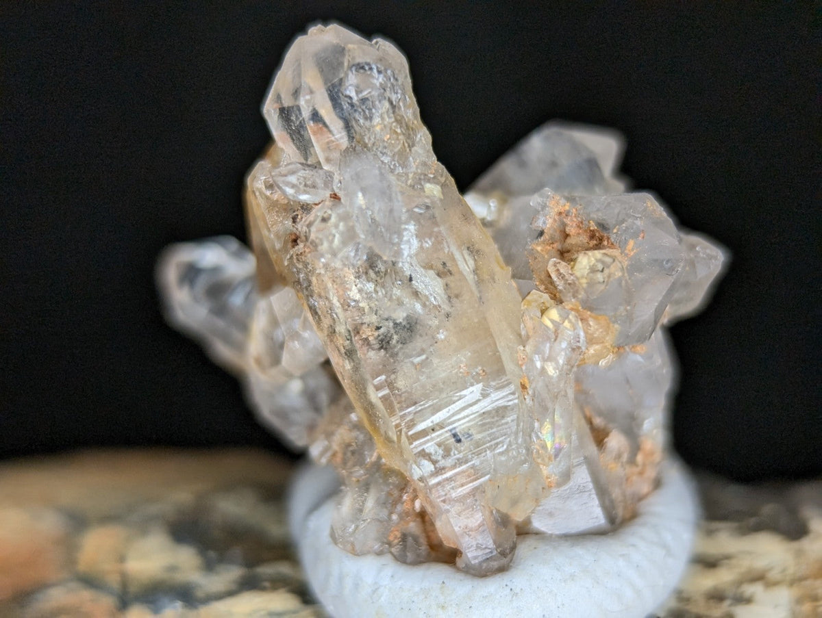 A clear quartz crystal cluster with golden mineral inclusions, displayed on a white circular base.
