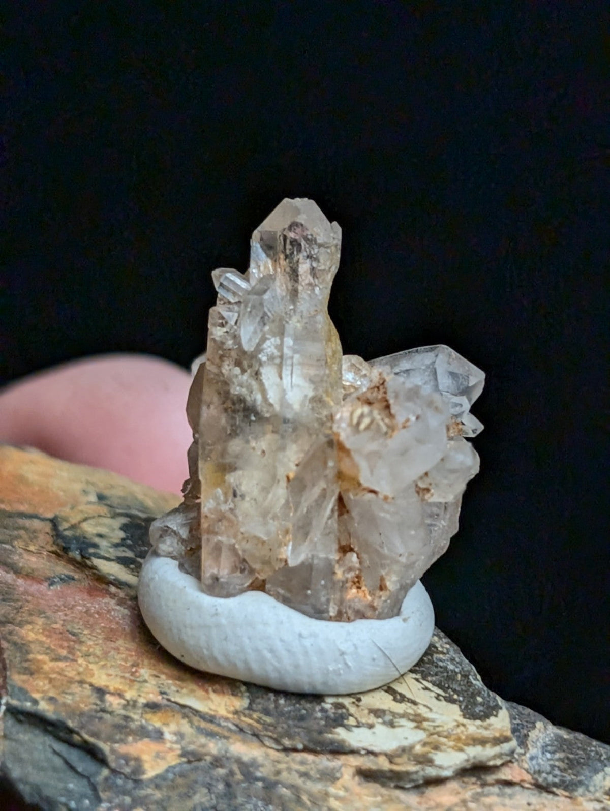 A translucent, multi-faceted quartz crystal cluster with subtle golden inclusions rests on a smooth white ceramic base.