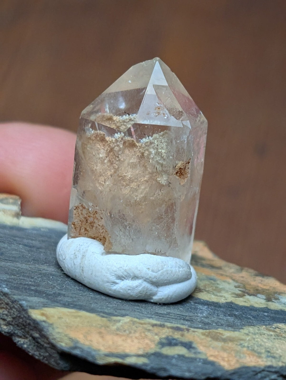 A clear quartz crystal with natural inclusions and a pointed top, resting on a white clay base.