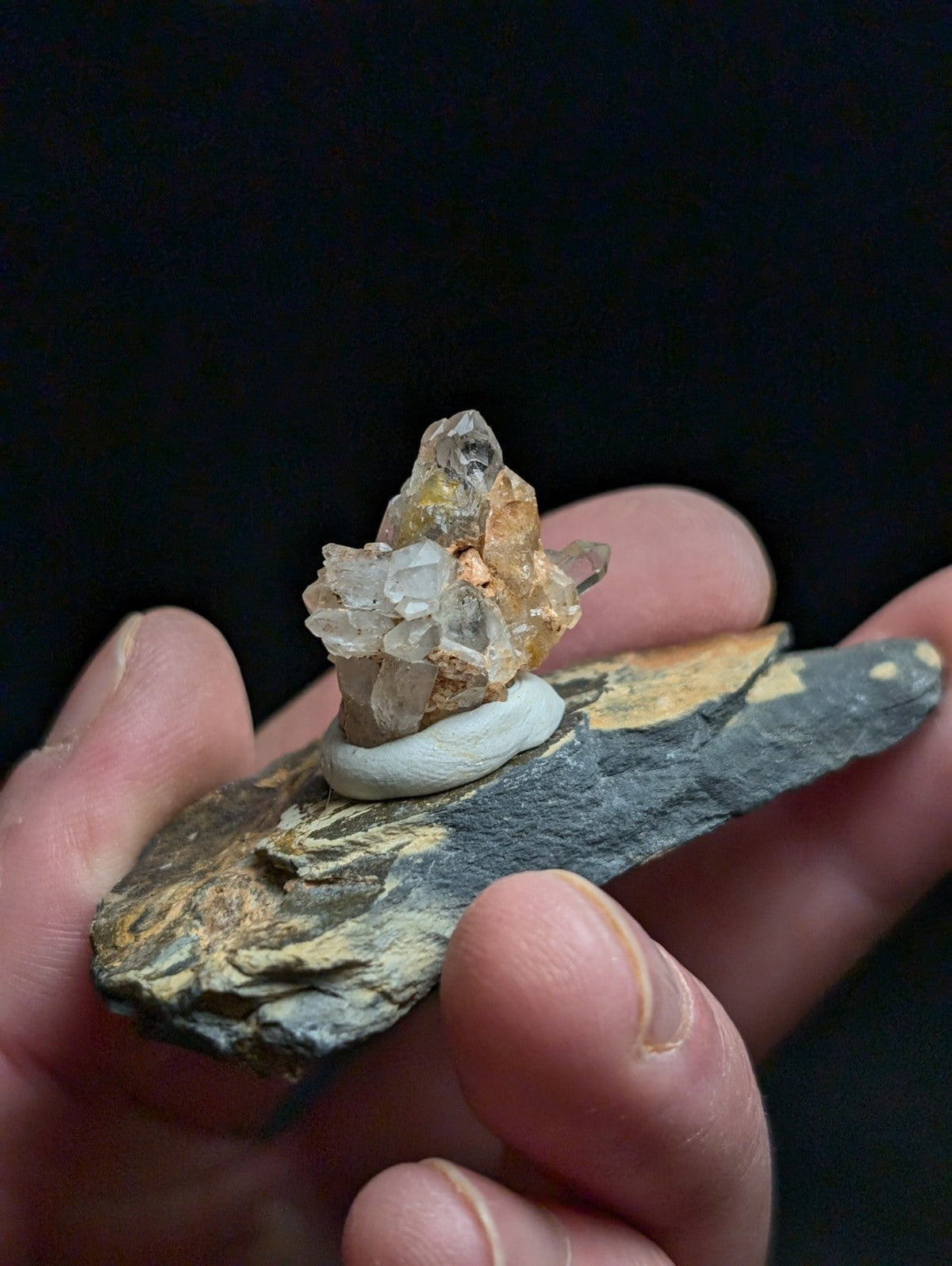 A delicate cluster of translucent quartz crystals with golden hues rests atop a smooth, dark gray stone base.