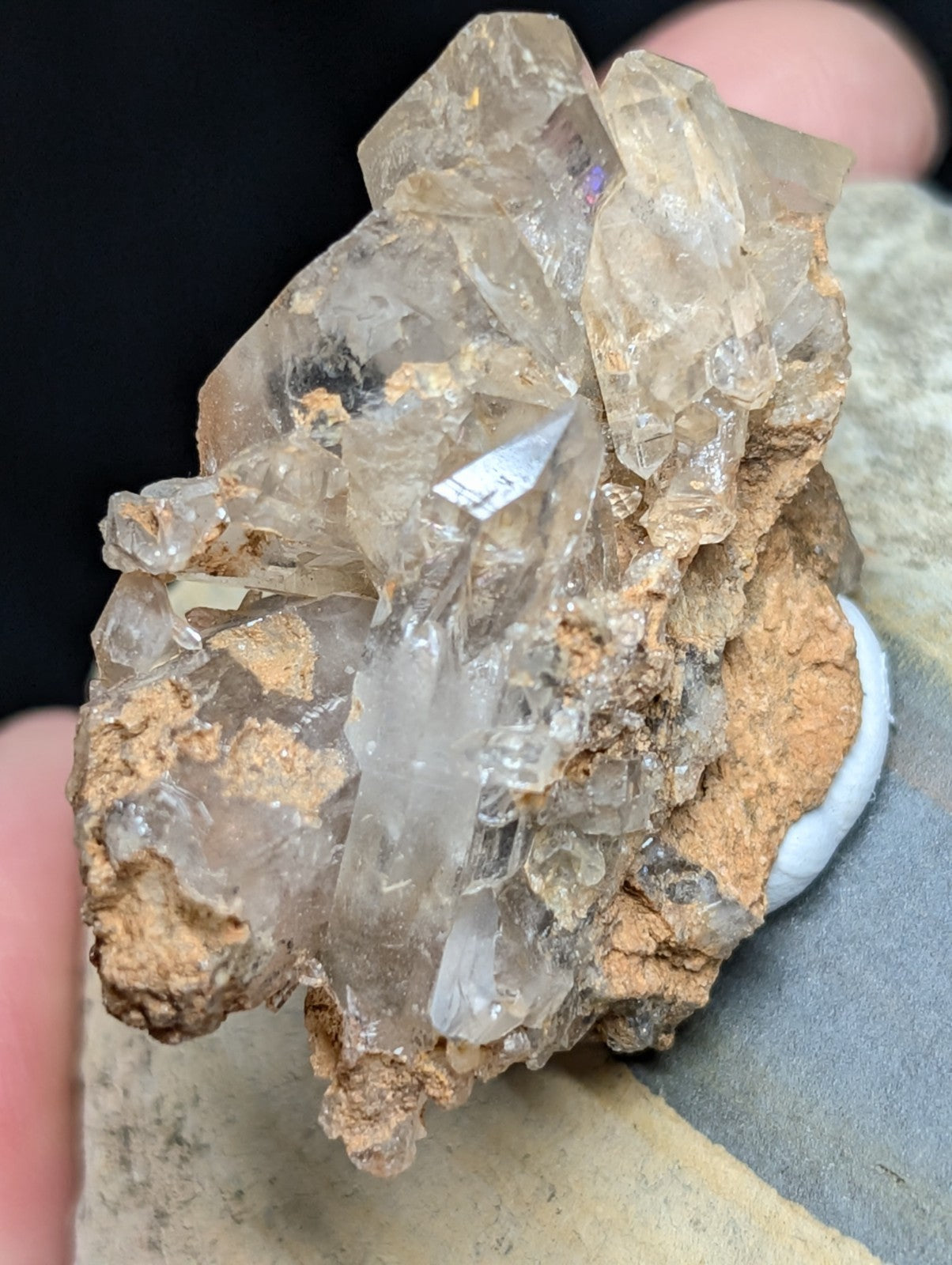 A cluster of translucent, clear quartz crystals with sharp facets and a slightly cloudy appearance, embedded in a rough brownish matrix.