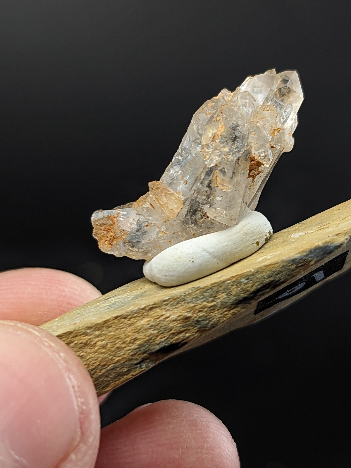 A translucent quartz crystal cluster with amber inclusions, resting atop a smooth white stone on a wooden tool.