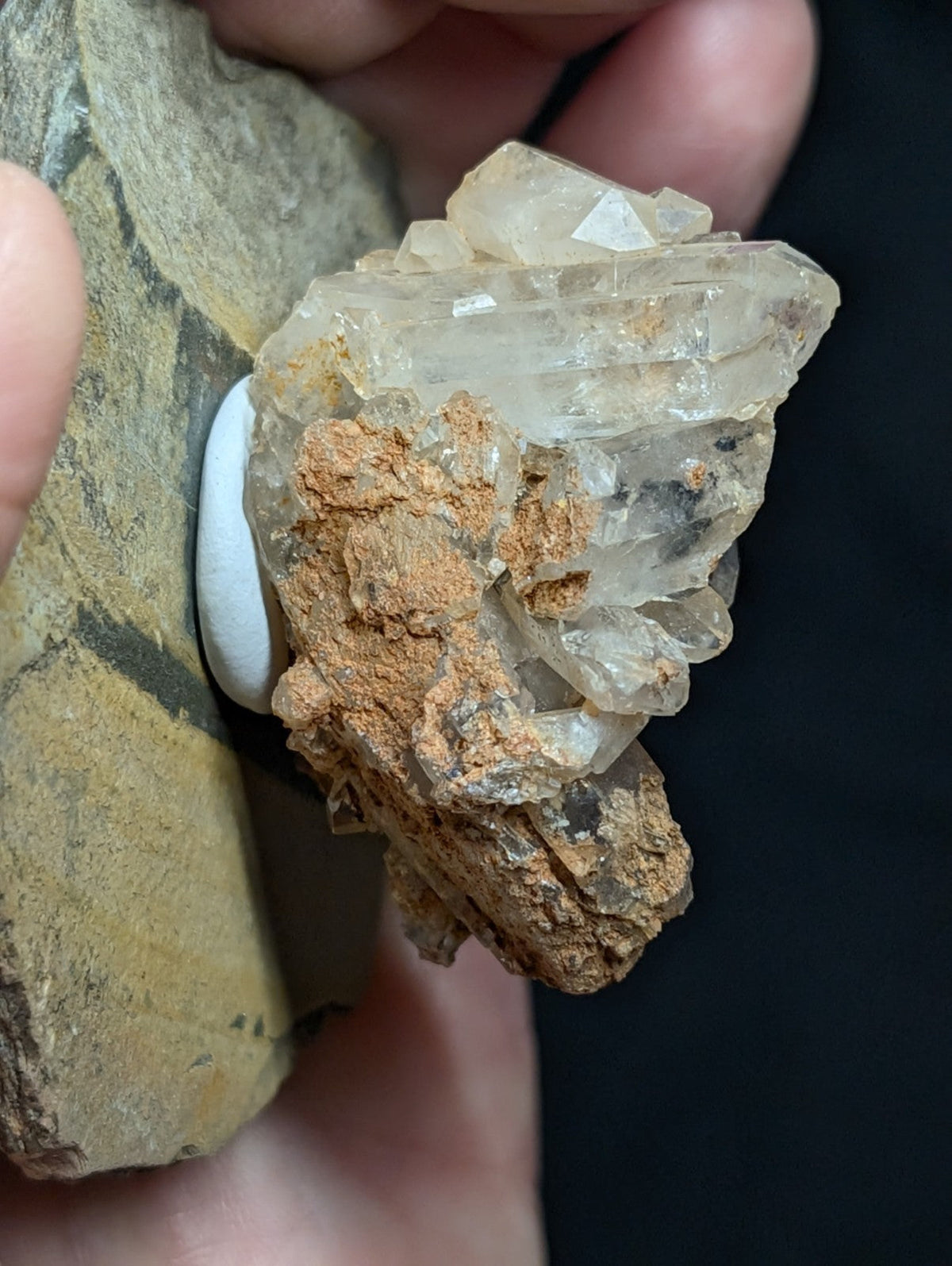A cluster of translucent, clear quartz crystals with a rough, earthy brown matrix holding them together.