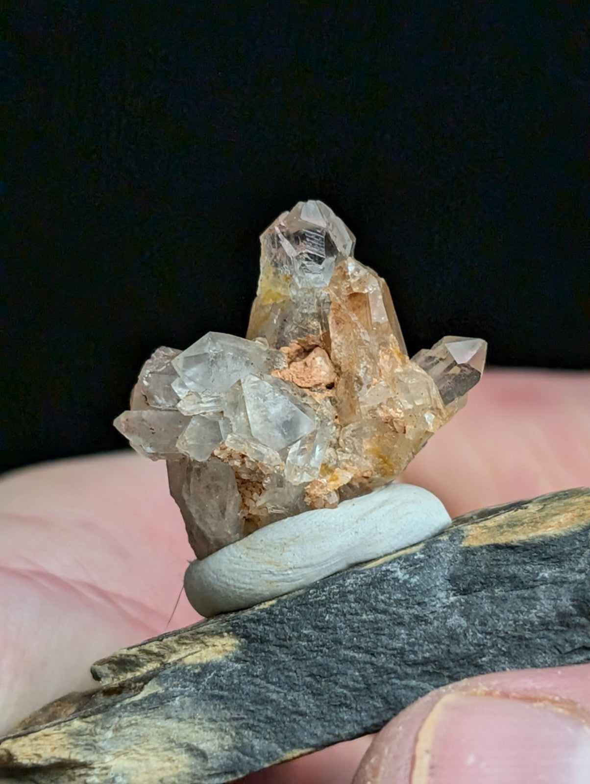 A translucent quartz crystal cluster with clear, faceted points and amber-tinted matrix held in a hand.