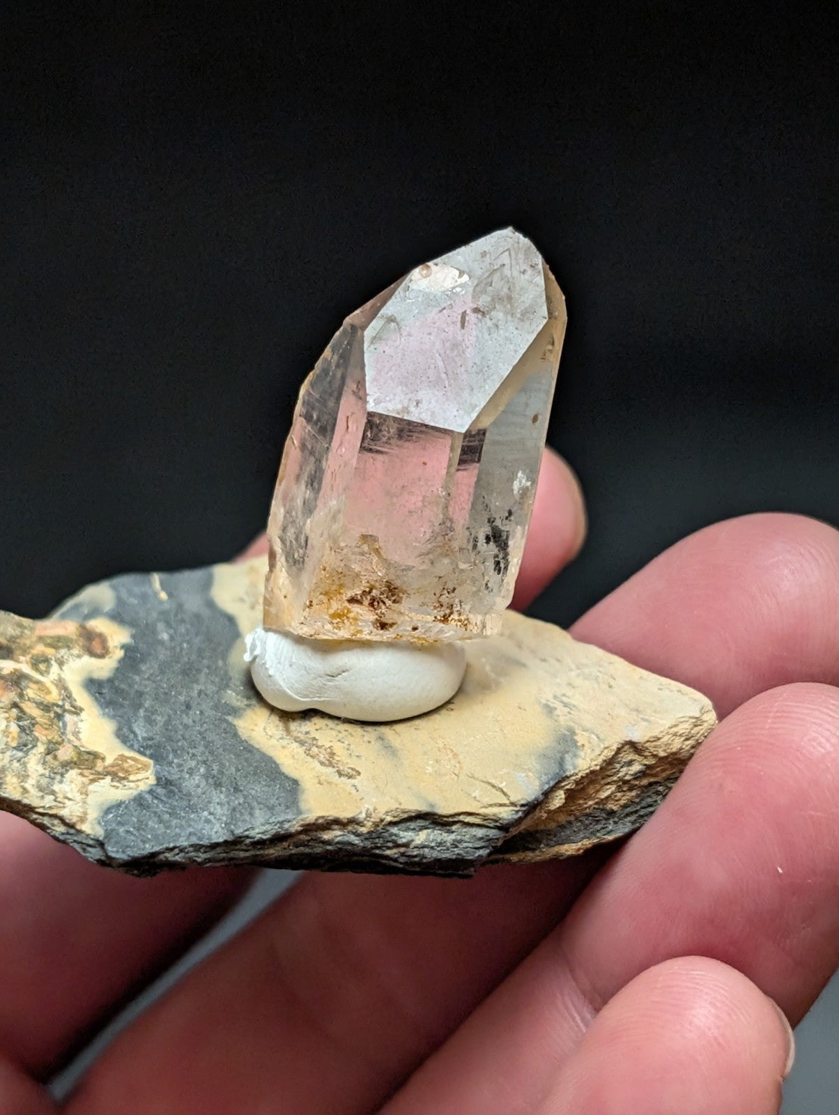A translucent, faceted quartz crystal with a subtle pink hue stands upright on a natural stone base.