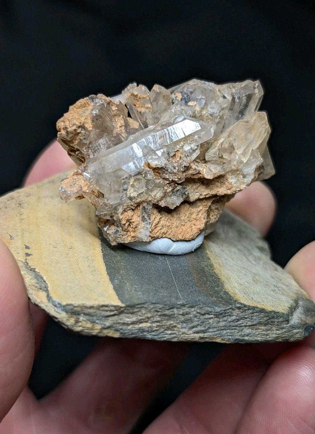 A cluster of translucent quartz crystals with a brownish matrix, mounted on a striped rock base.