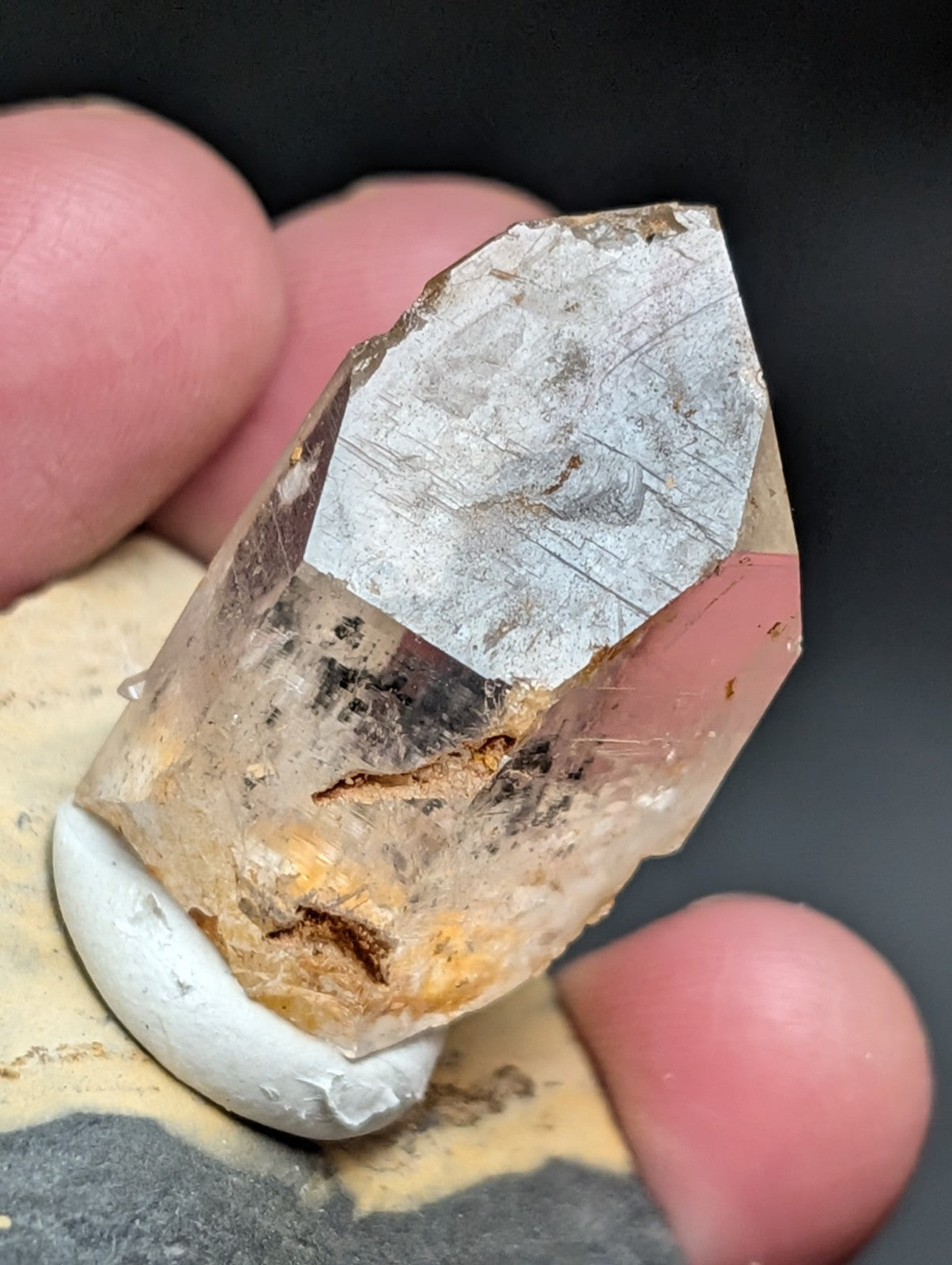 A translucent quartz crystal with a pointed, faceted top and natural inclusions of brownish-orange mineral streaks.