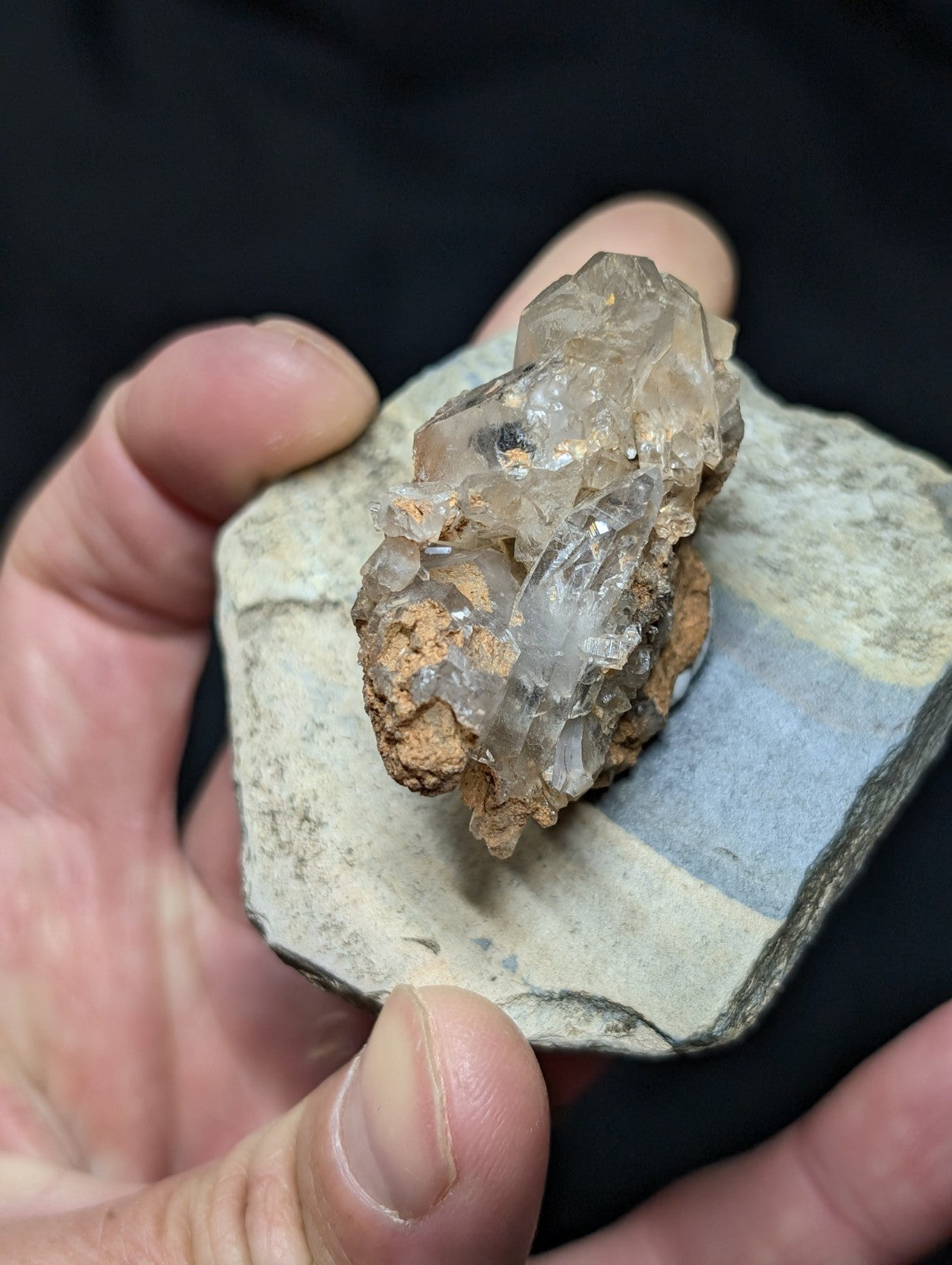A translucent quartz crystal cluster with a rough, earthy base rests on a flat stone slab.