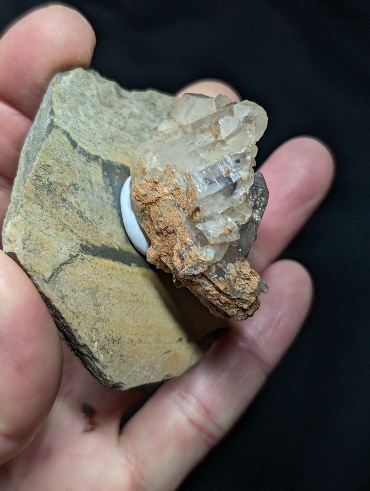 A cluster of translucent, crystalline quartz formations emerging from a rough, earthy-toned rock matrix.