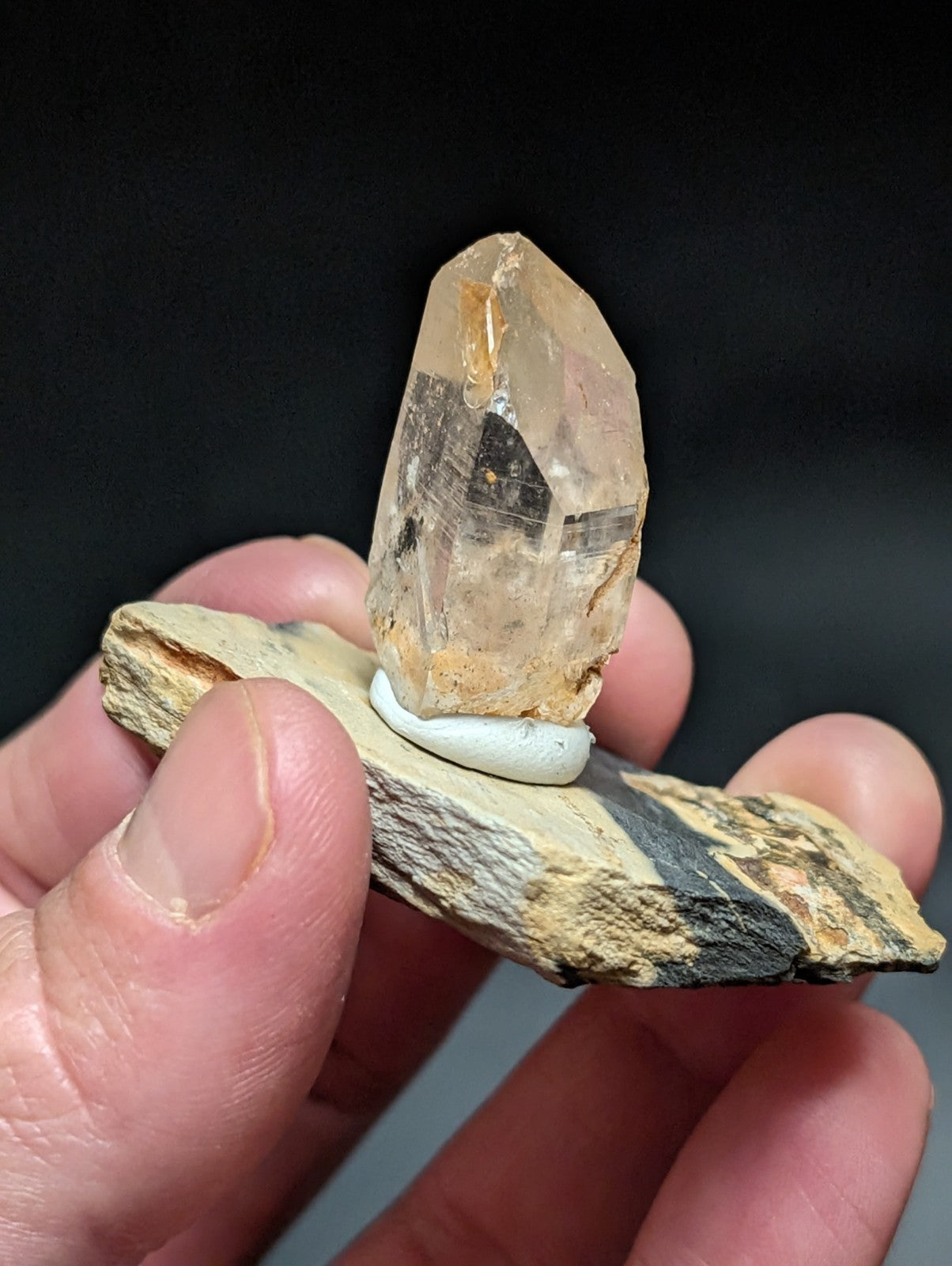 A translucent, amber-hued quartz crystal with visible internal inclusions and a pointed tip rests atop a small white circular base.