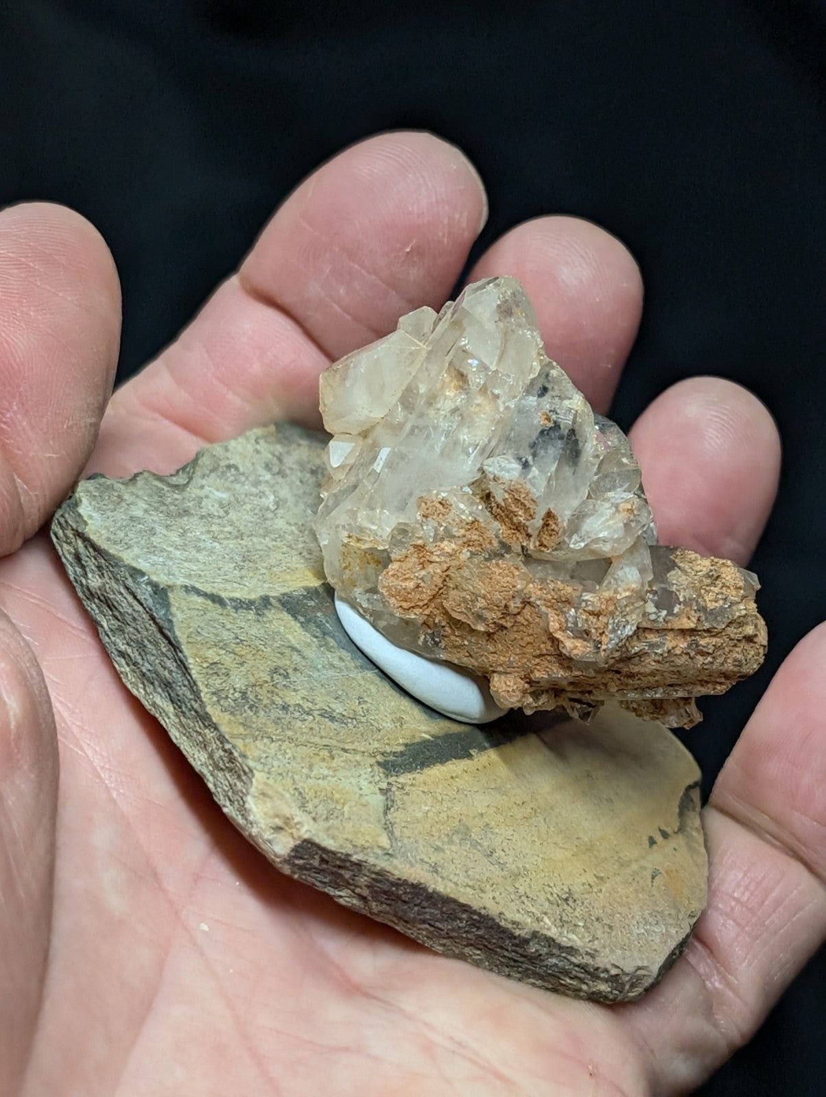 A translucent, crystalline mineral specimen with a rough, earthy brown matrix and clear facets rests on a flat, greenish-yellow rock base.