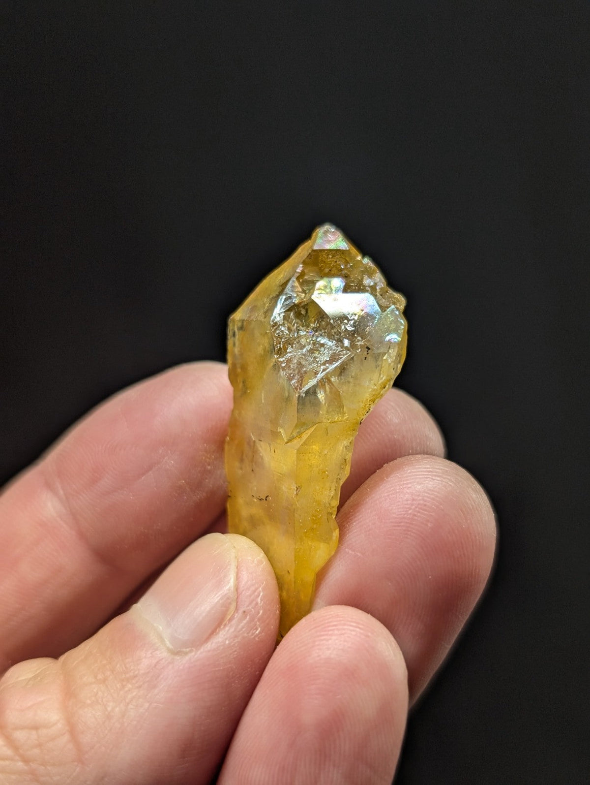 A translucent yellow crystal with a pointed, faceted tip and subtle iridescent highlights.