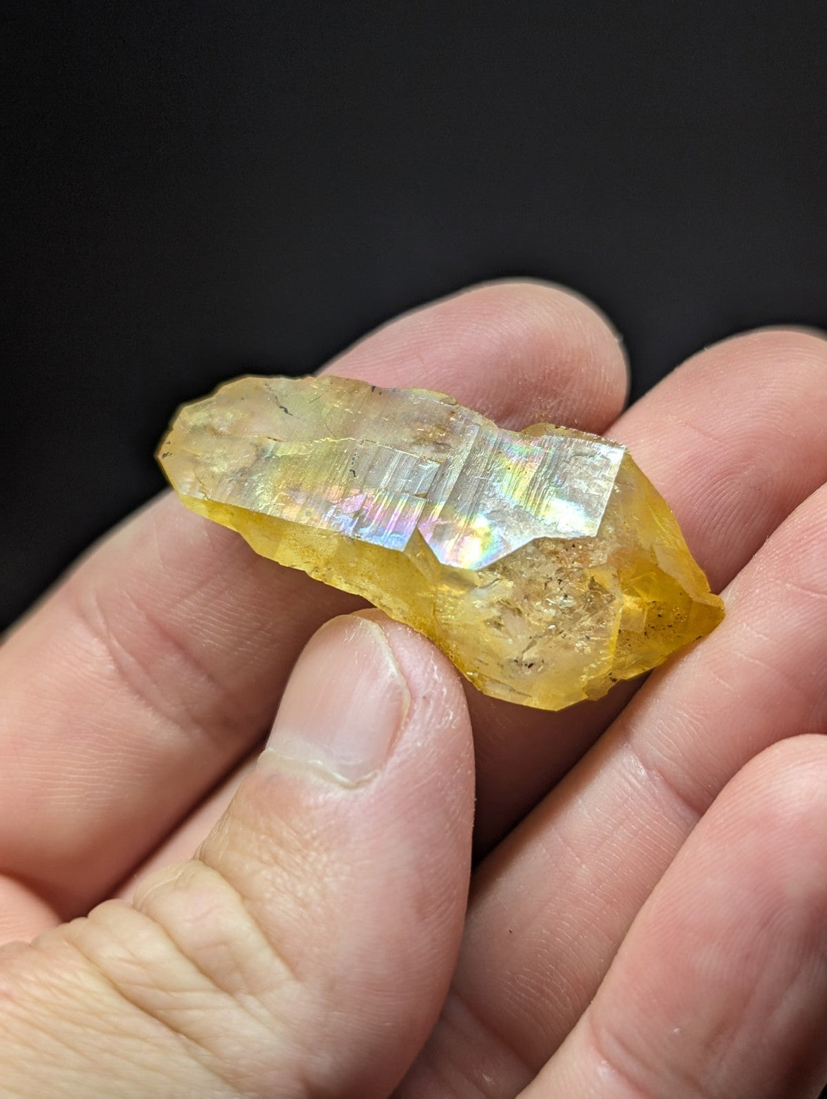 A translucent yellow crystal with iridescent facets, held gently in a hand.
