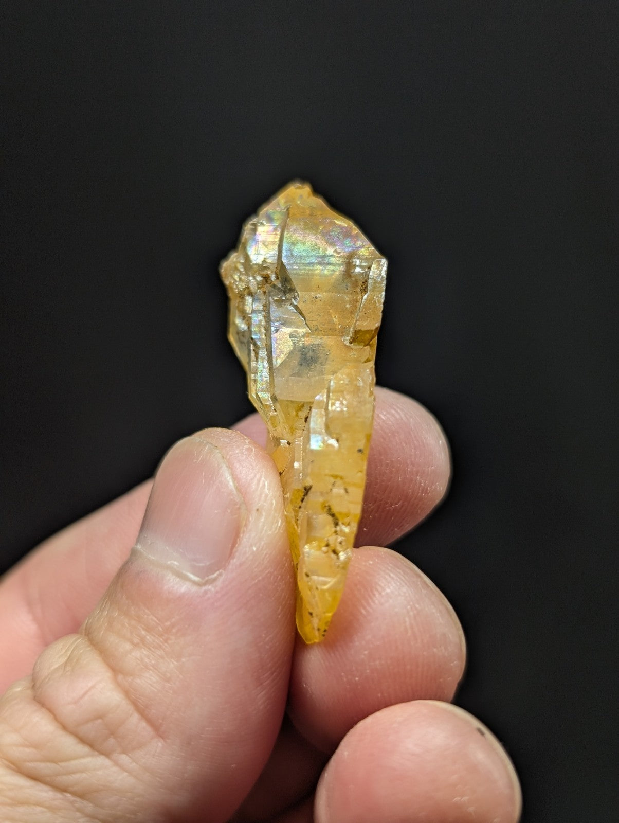 A translucent yellow crystal with iridescent facets, held gently between fingers.