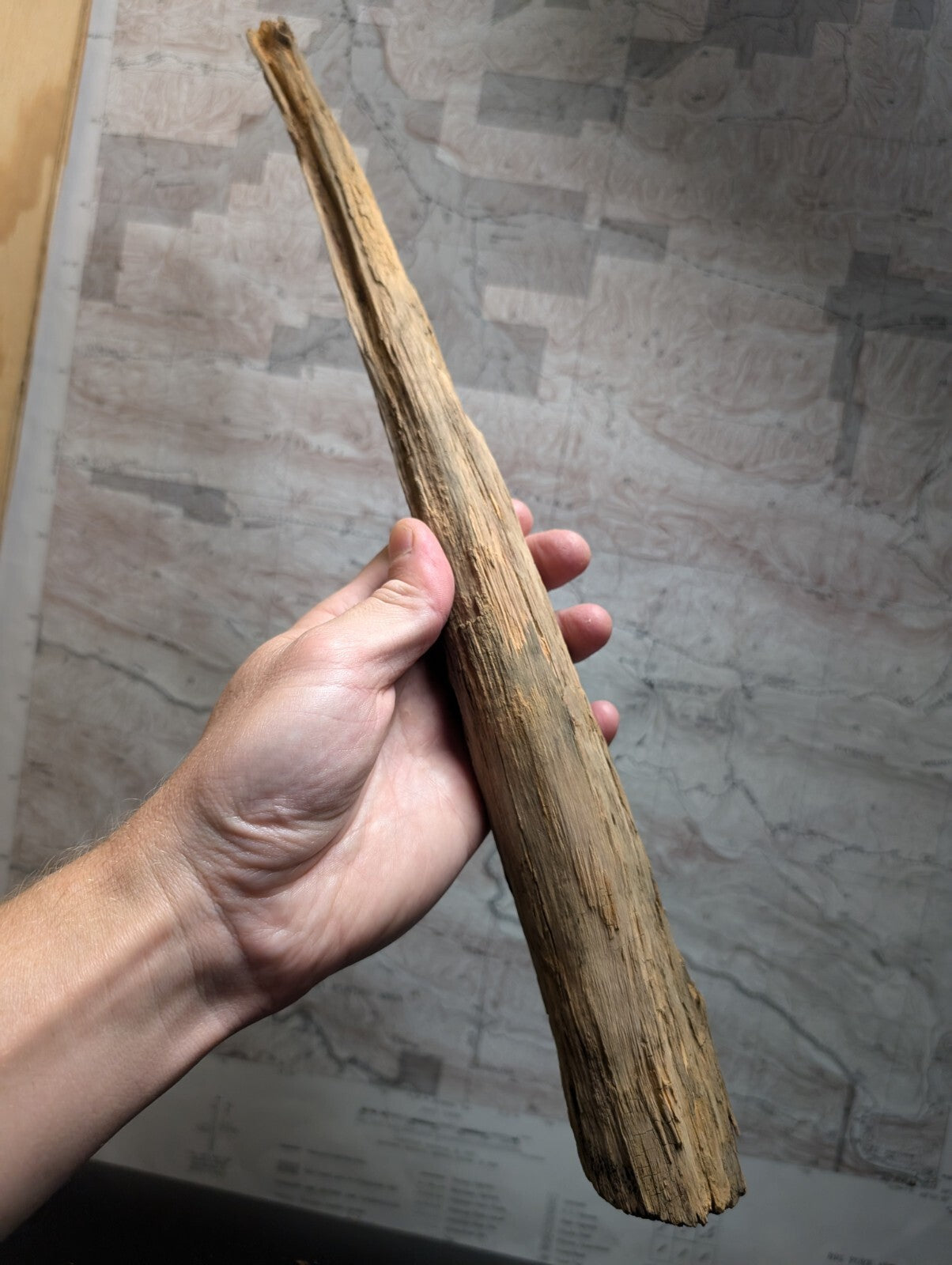 A weathered, light brown wooden stick with a rough texture and natural grain.