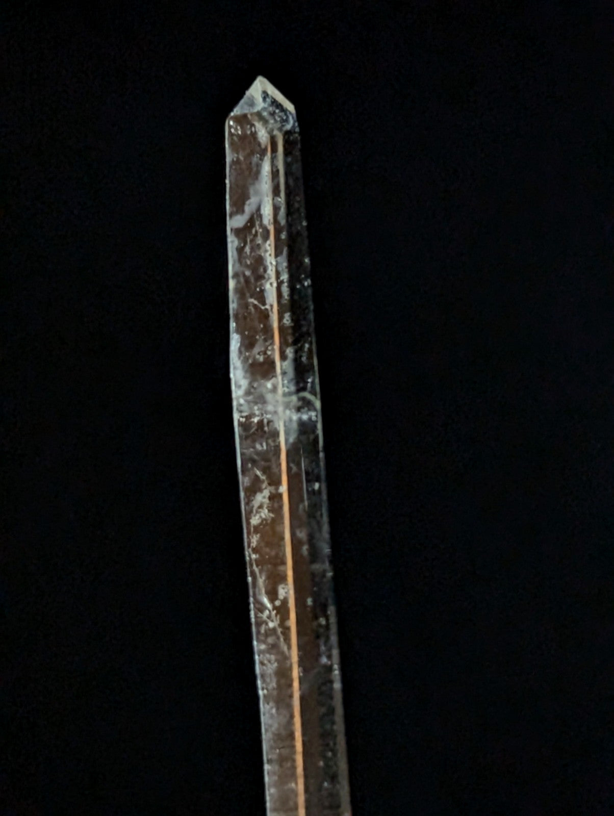 A clear quartz crystal with a pointed tip and natural internal inclusions, featuring subtle golden streaks running along its length.