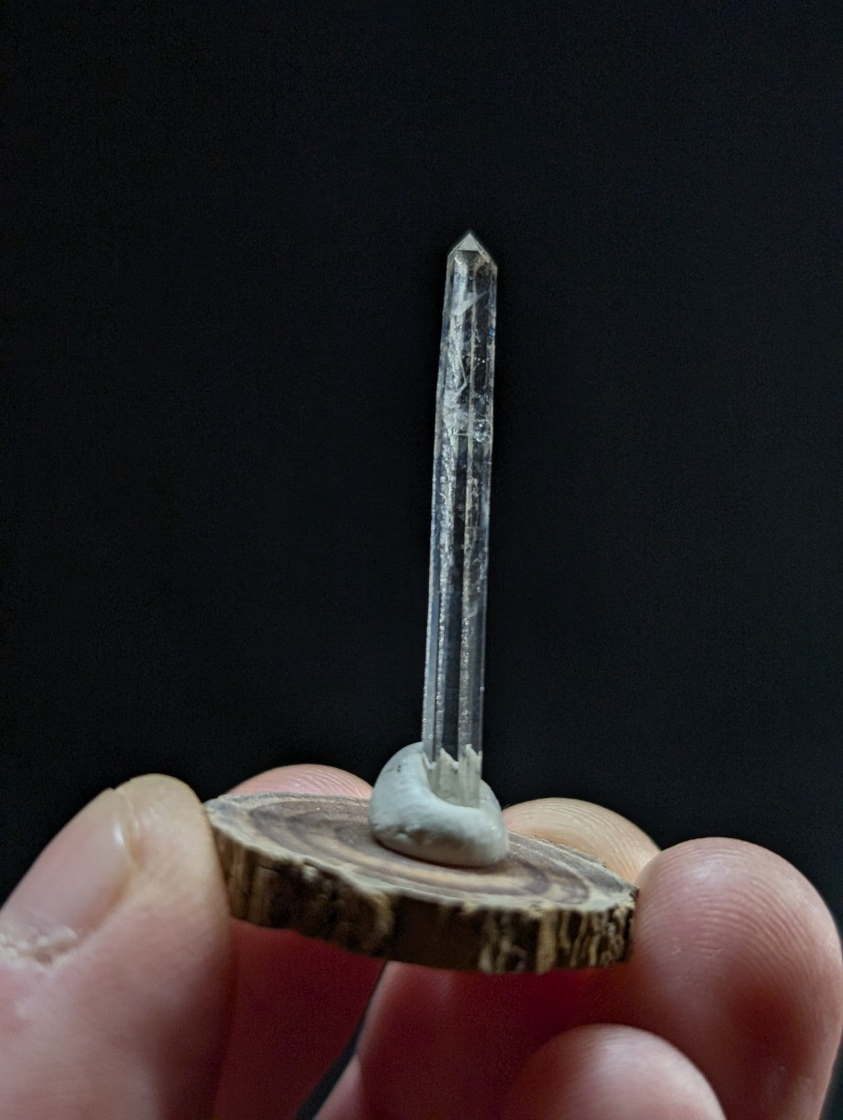 A clear quartz crystal with a pointed tip, mounted on a circular wooden base.