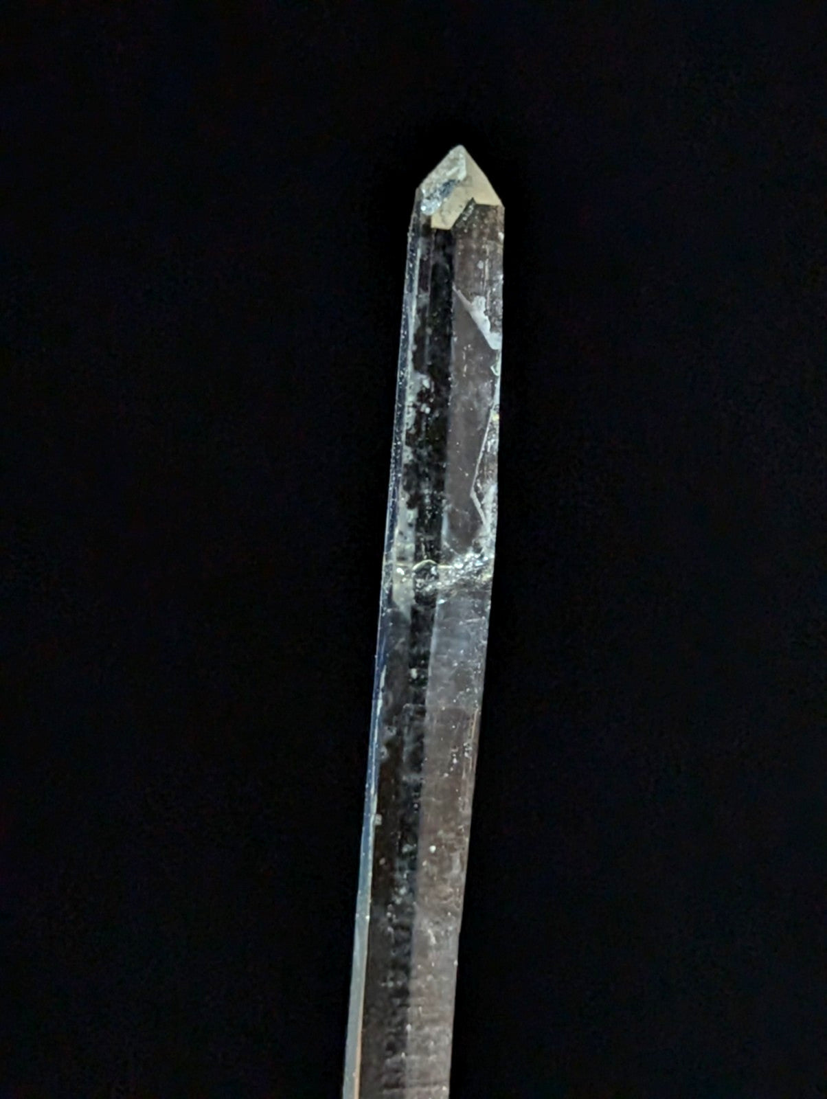 A translucent quartz crystal with a pointed tip and natural inclusions running vertically along its length.