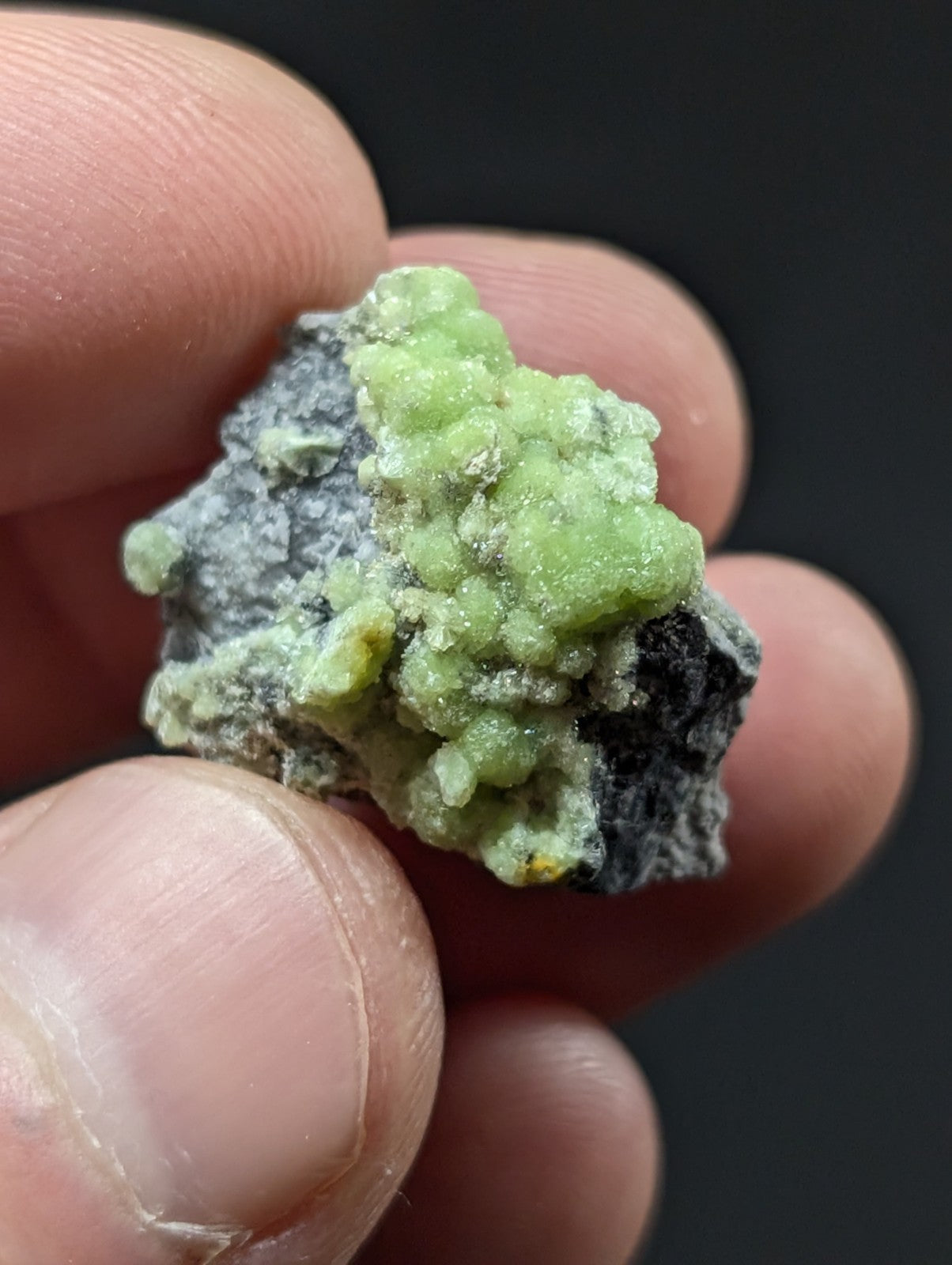 A vibrant green, crystalline mineral specimen with a rough, textured surface and patches of gray matrix.