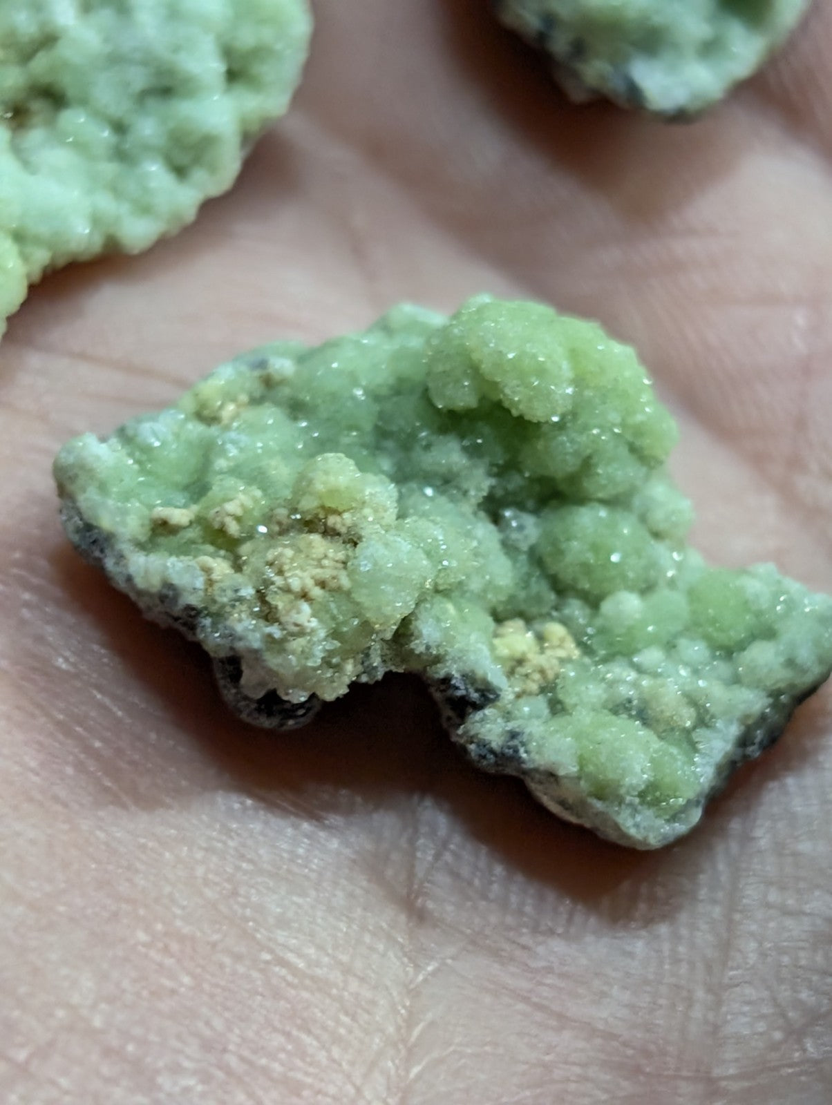 A pale green, crystalline mineral specimen with a rough, textured surface and small yellowish patches.