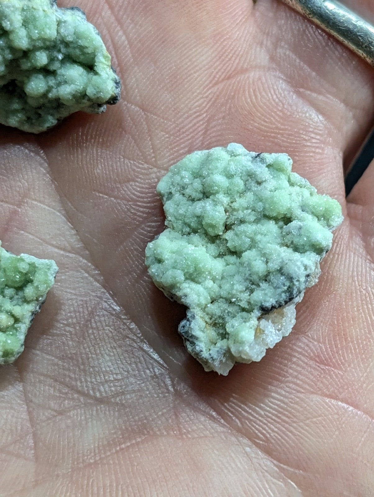 A pale green, crystalline mineral specimen with a rough, textured surface and subtle darker patches.