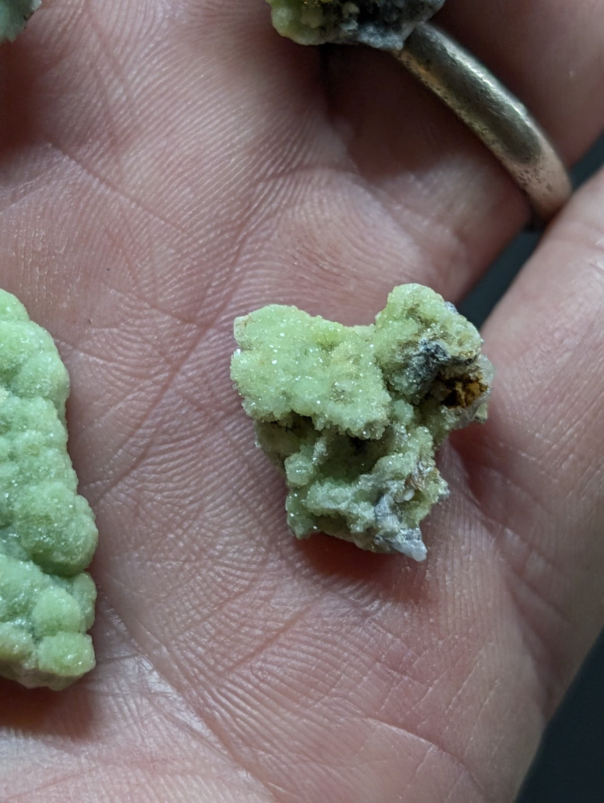 A rough, pale green mineral specimen with a crystalline texture and some darker inclusions.