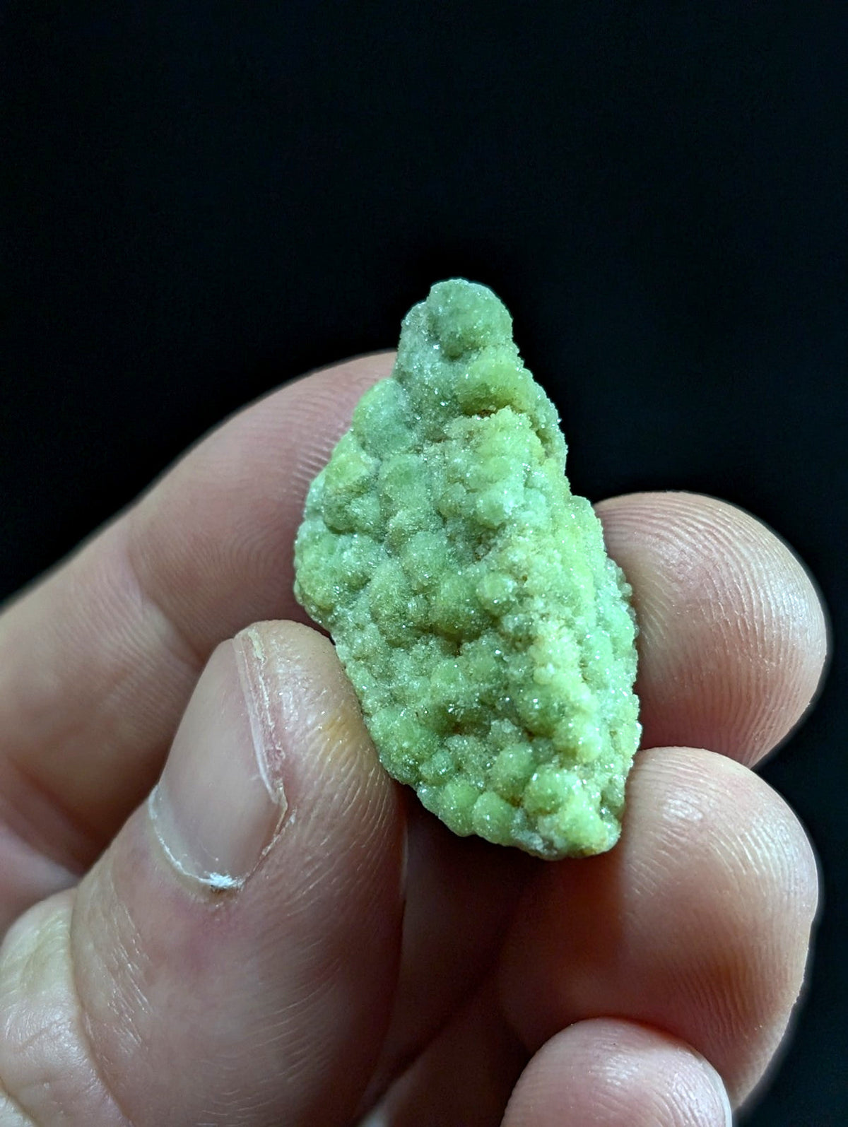 A pale green, textured mineral specimen with a rough, bumpy surface held gently in someone’s hand.