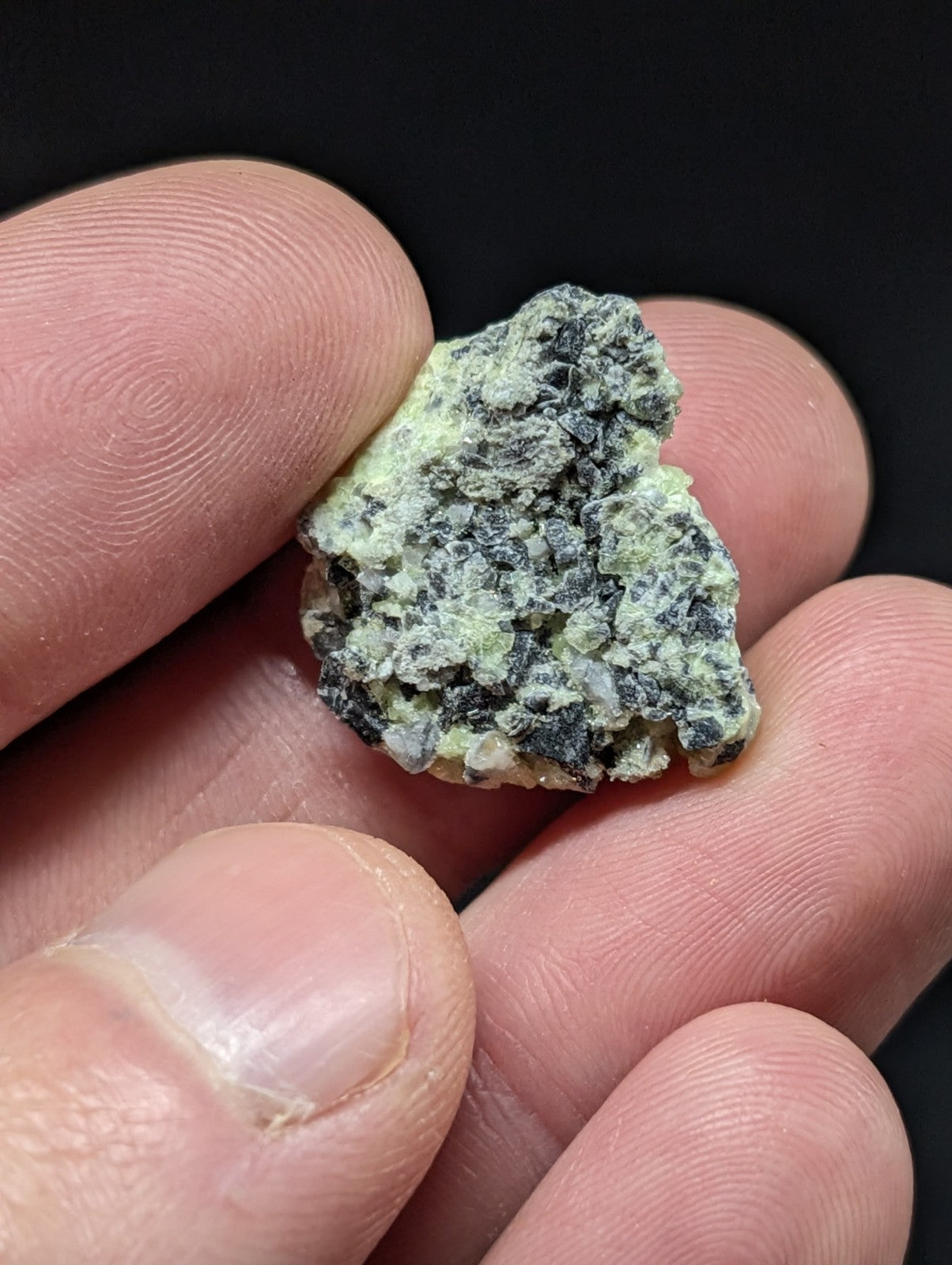 A rough, irregularly shaped mineral specimen with a mottled green and dark gray surface.
