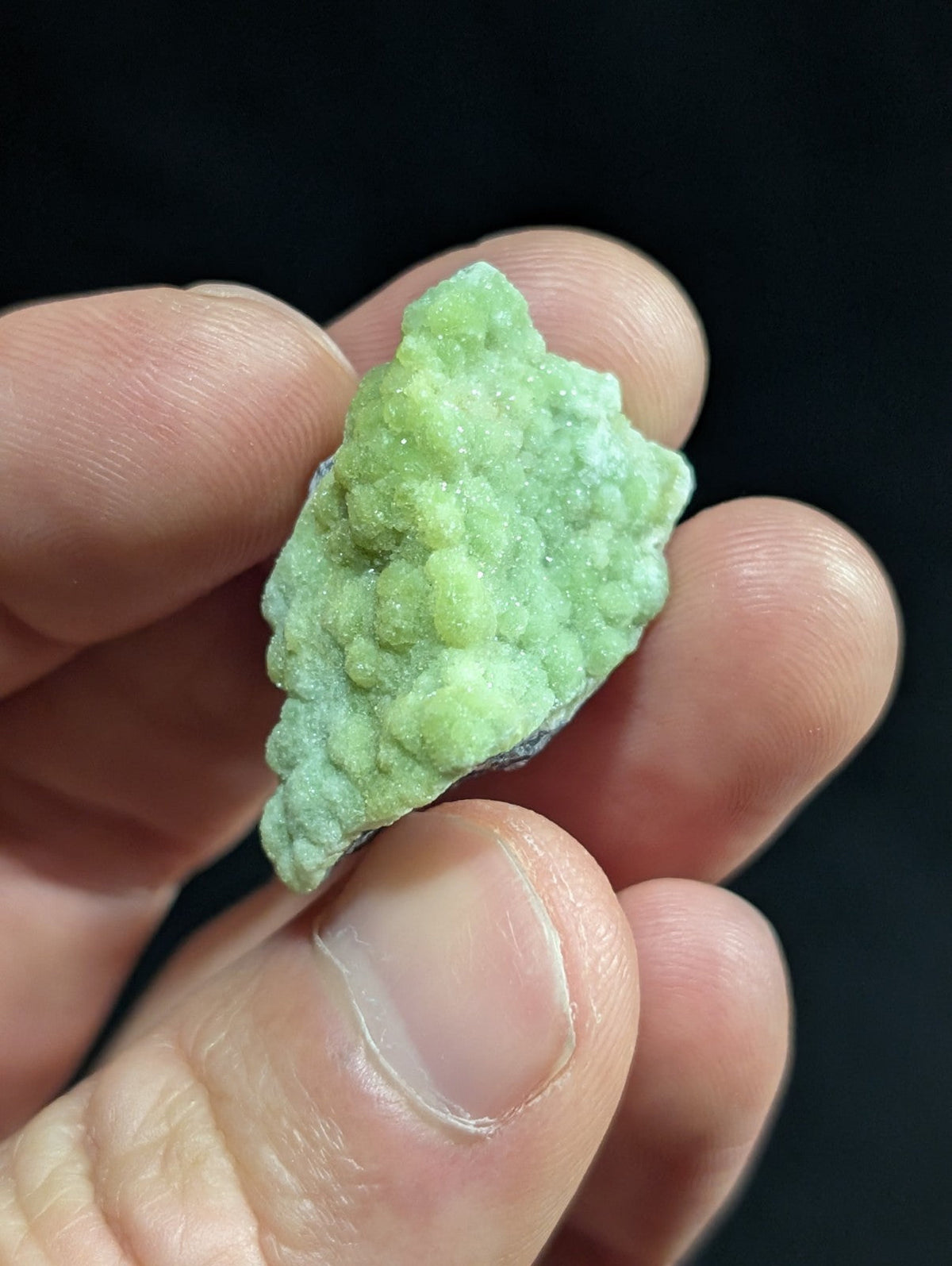 A textured, light green mineral specimen with a rough, crystalline surface held gently in someone’s hand.