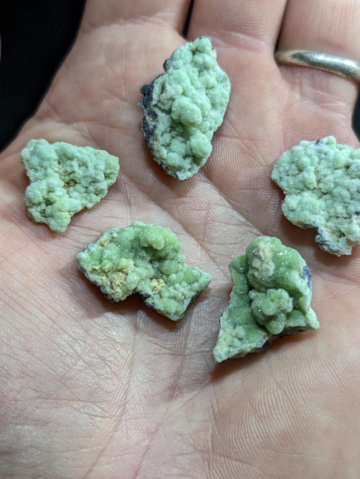 Light green, rough-textured mineral specimens with speckles of darker hues resting in an open palm.