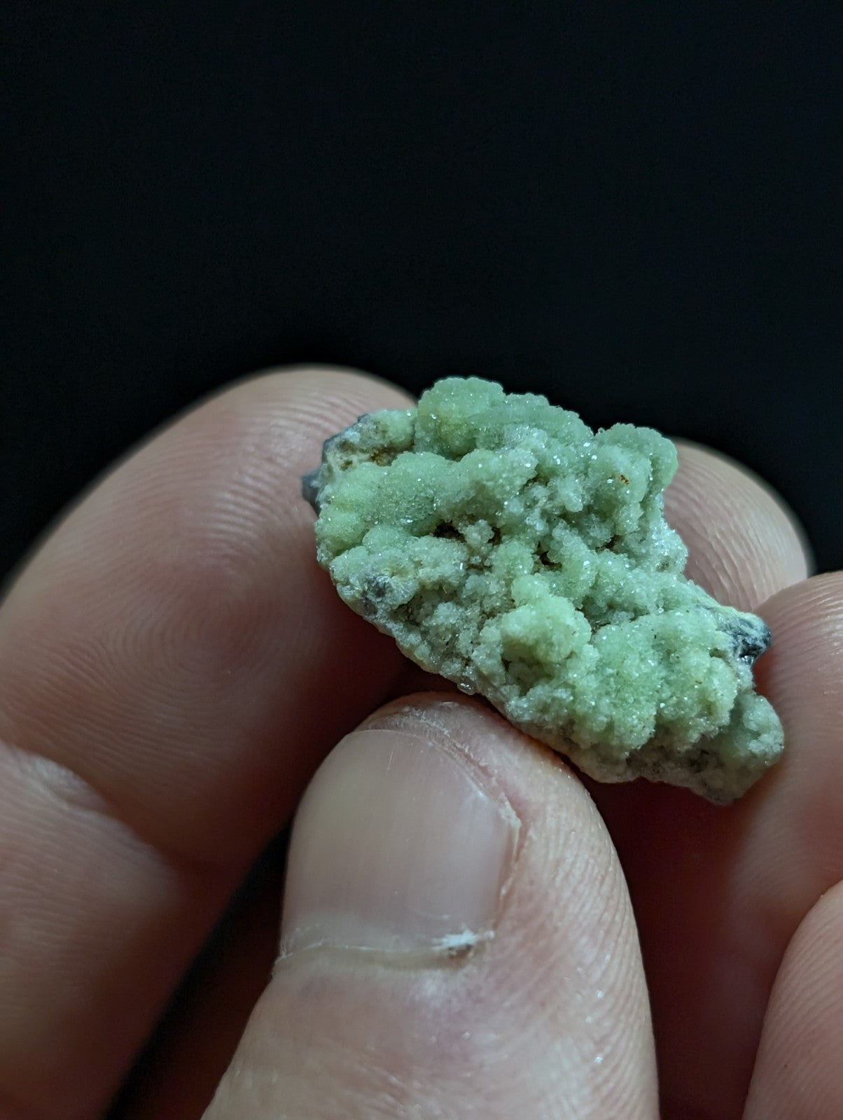 A textured, light green mineral specimen with a crystalline surface held between fingers.