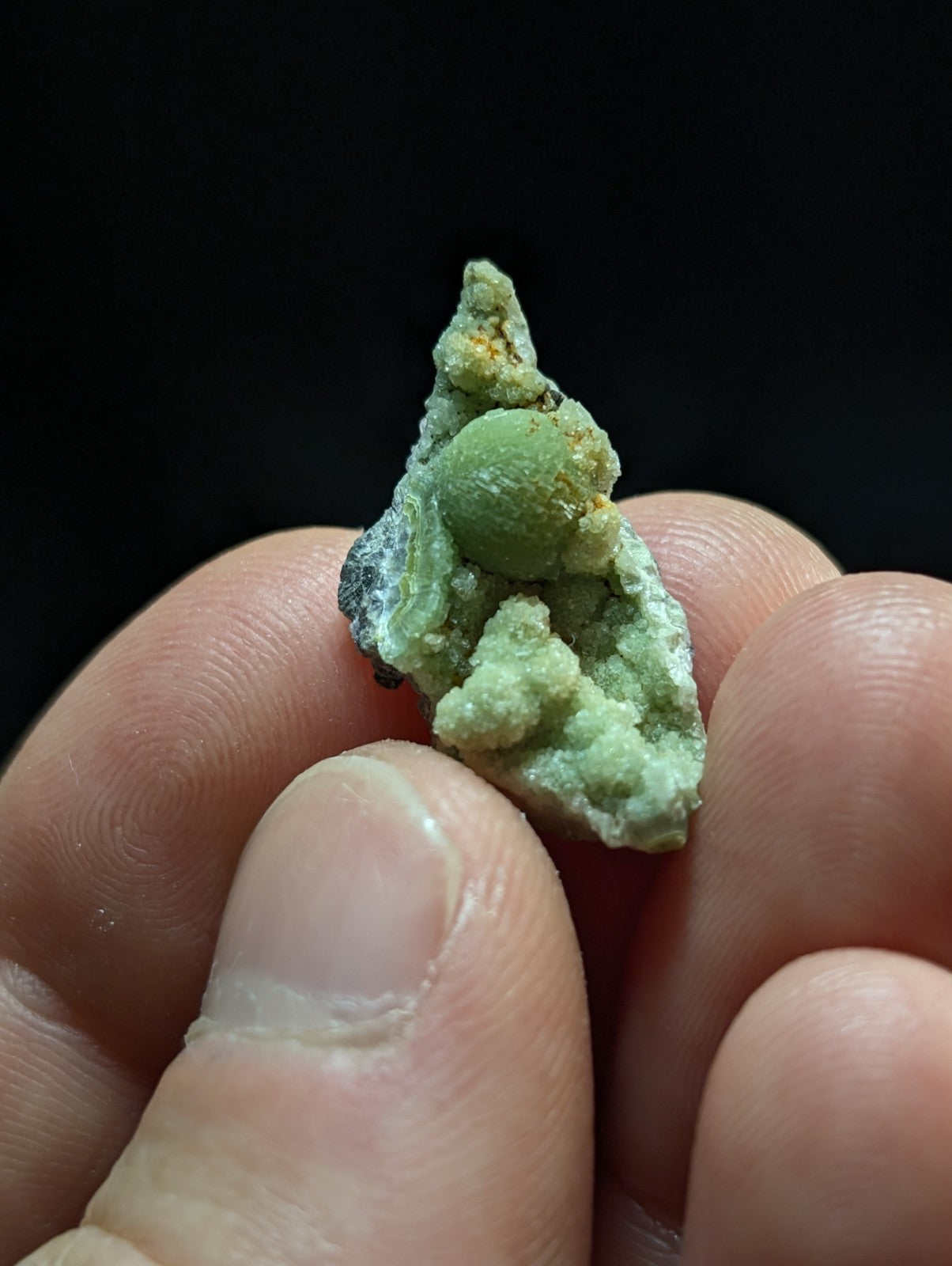 A small, light green spherical mineral specimen nestled within a rougher, textured matrix of the same hue.
