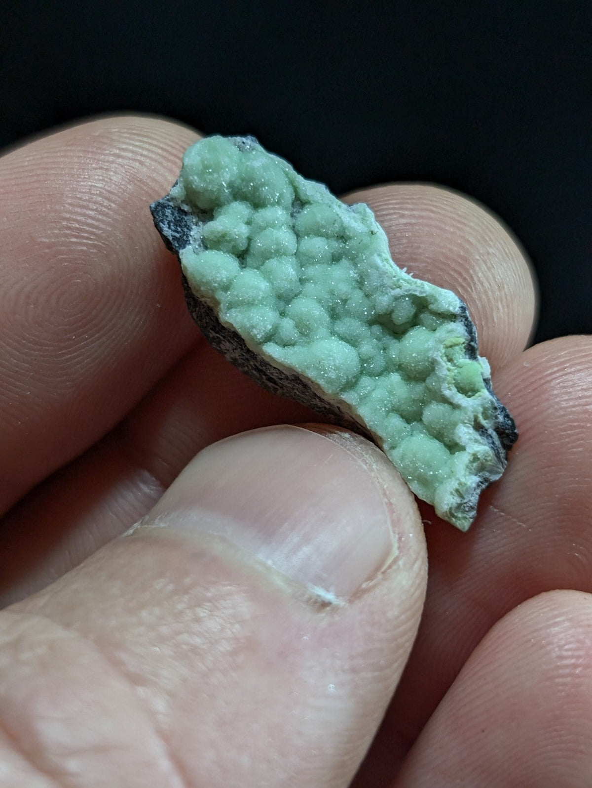 A vibrant green, crystalline mineral specimen with a textured surface and dark matrix.