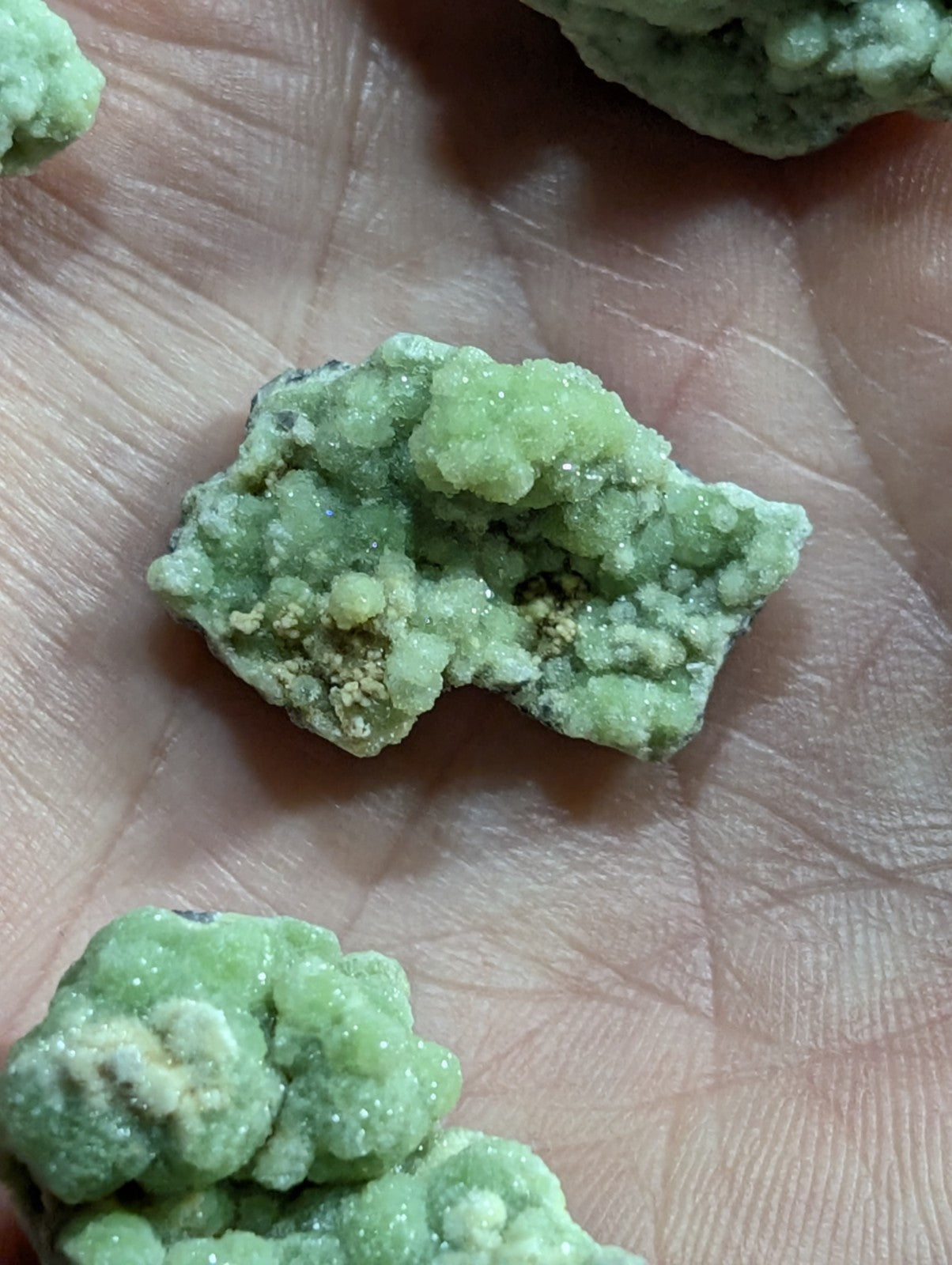 A rough, light green mineral specimen with a crystalline texture and speckles of yellowish material.