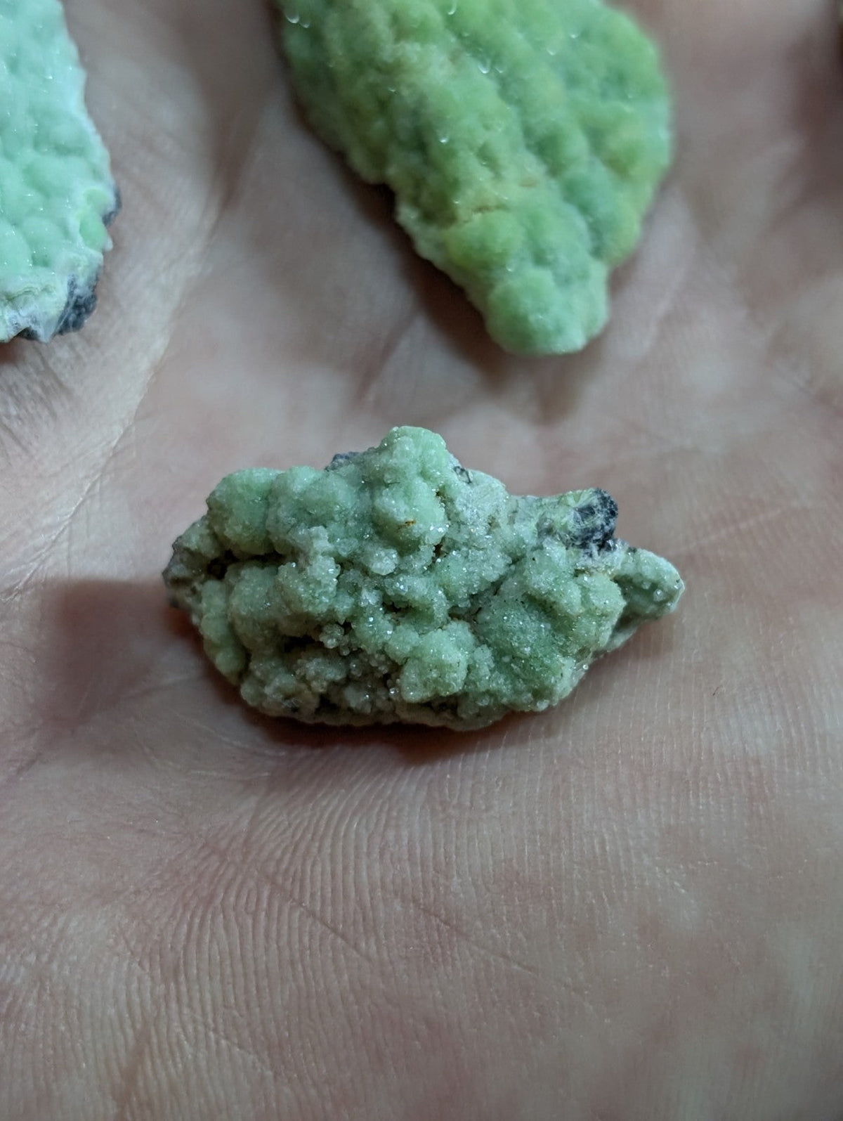 A rough, light green mineral specimen with a textured, crystalline surface and small dark inclusions.
