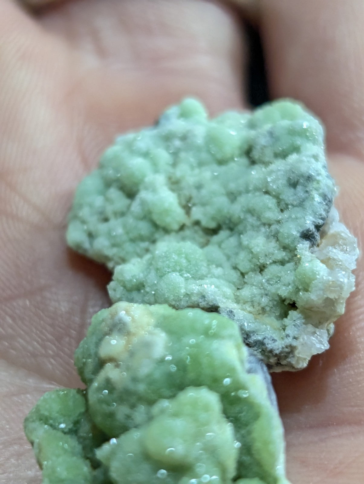 A rough, light green mineral specimen with a textured, crystalline surface and some white veining.