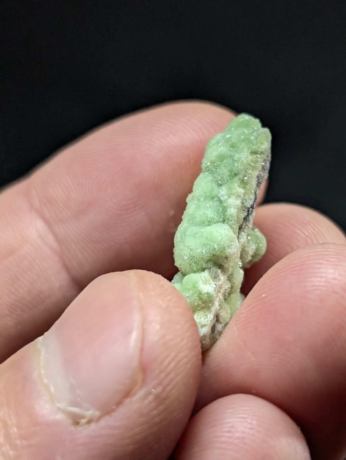 A textured, light green mineral specimen with a rough, bumpy surface held between fingers.
