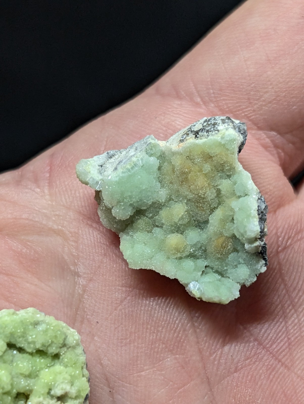 A pale green, crystalline mineral specimen with a rough, textured surface and small yellowish nodules embedded within it.