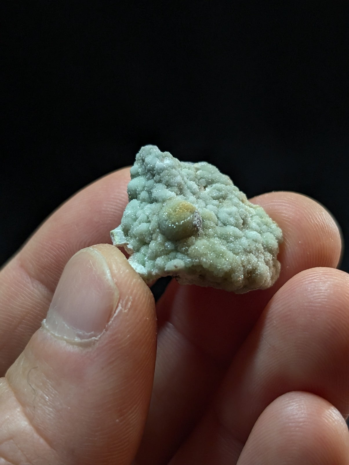 A textured, light green mineral specimen with a rough, bumpy surface and a small yellowish inclusion.