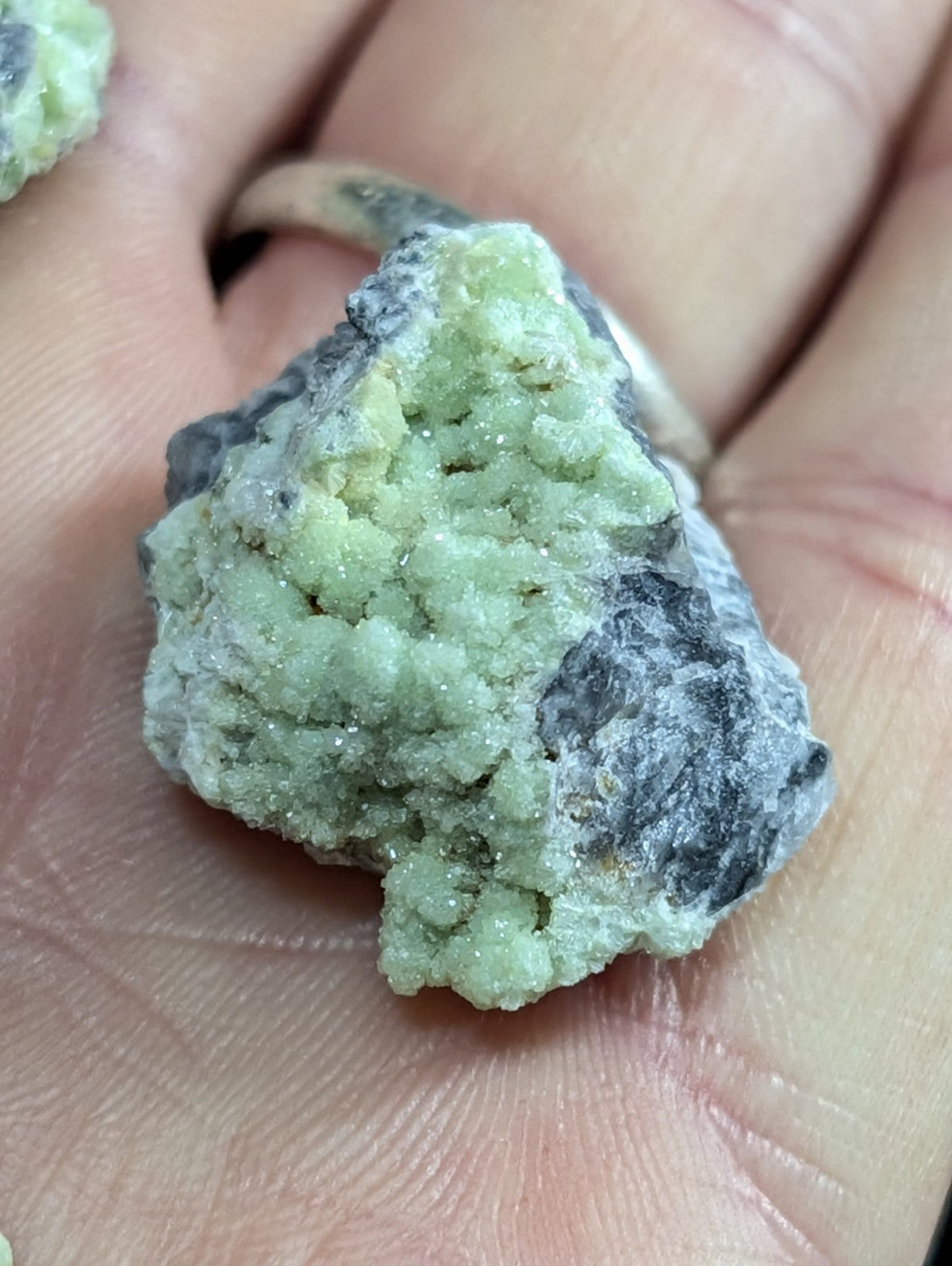 A rough, light green mineral specimen with a crystalline texture and dark gray matrix.