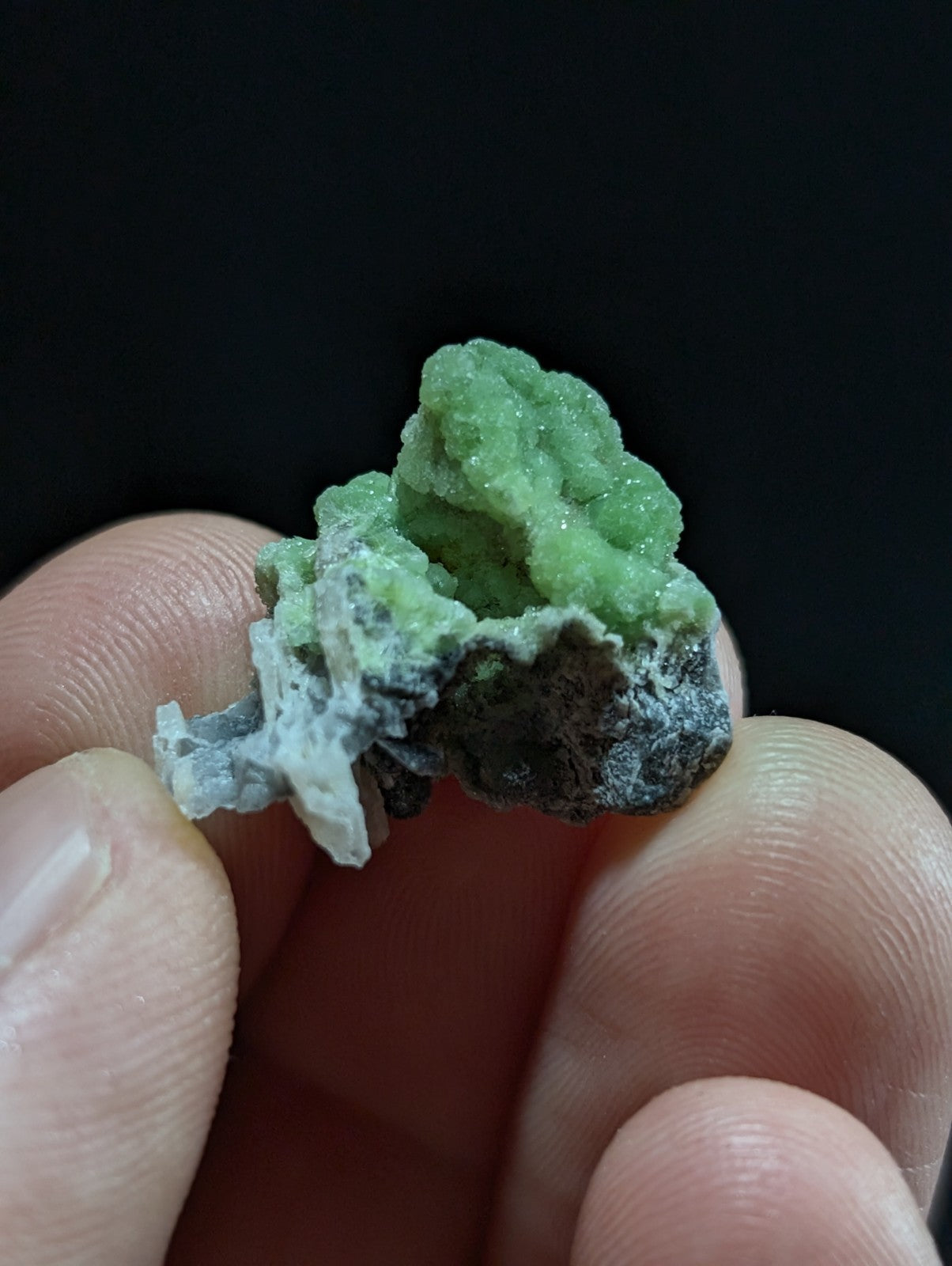 A vibrant green, crystalline mineral specimen with a rough, textured surface and dark gray matrix.