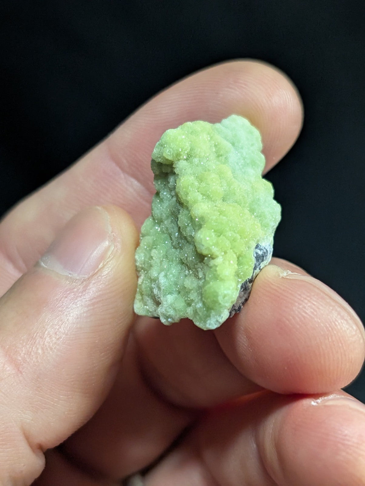A pale green, textured mineral specimen with a crystalline surface held between fingers.