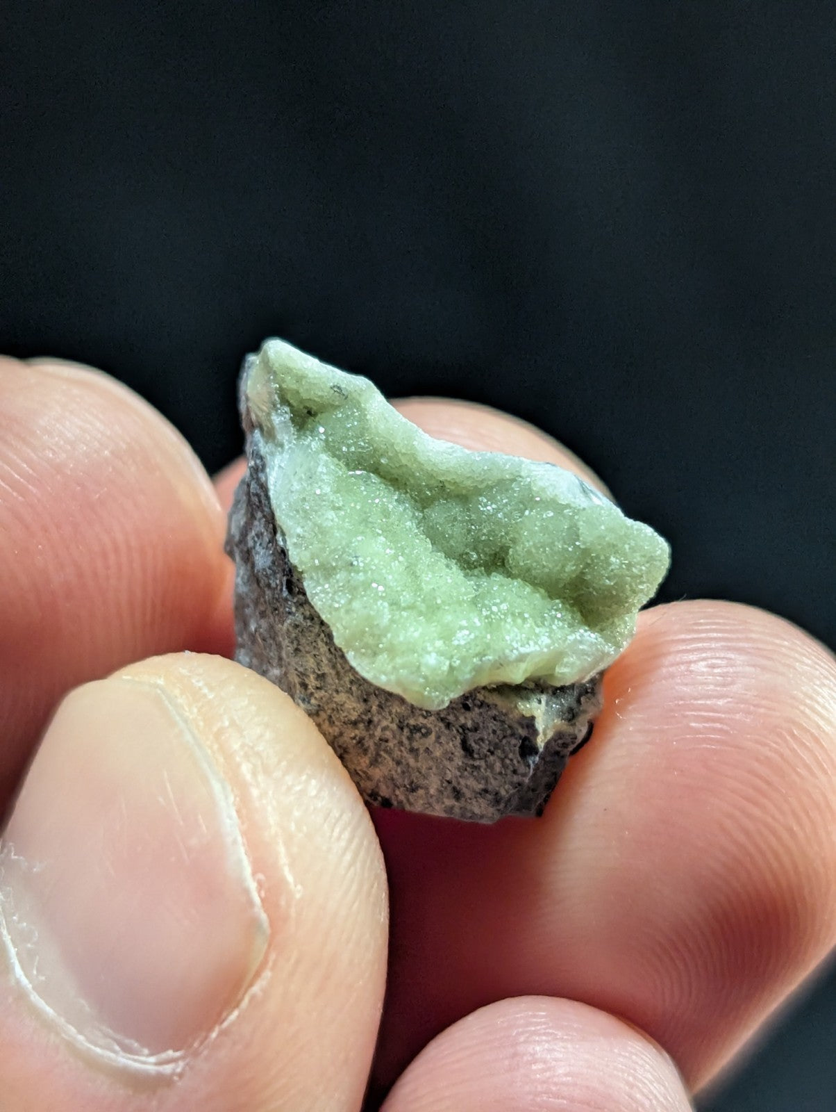 A delicate, pale green crystalline mineral specimen with a textured surface and translucent quality.