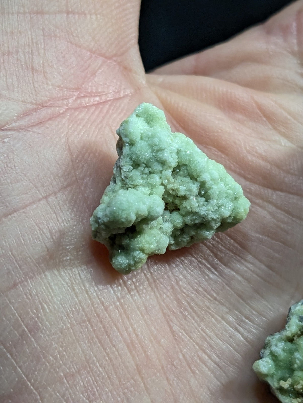 A rough, light green mineral specimen with a crystalline texture rests in the palm of a hand.